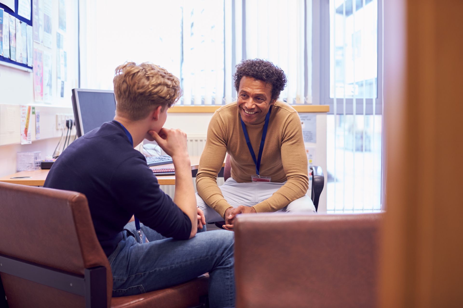 A man is sitting in a chair talking to another man in a room.