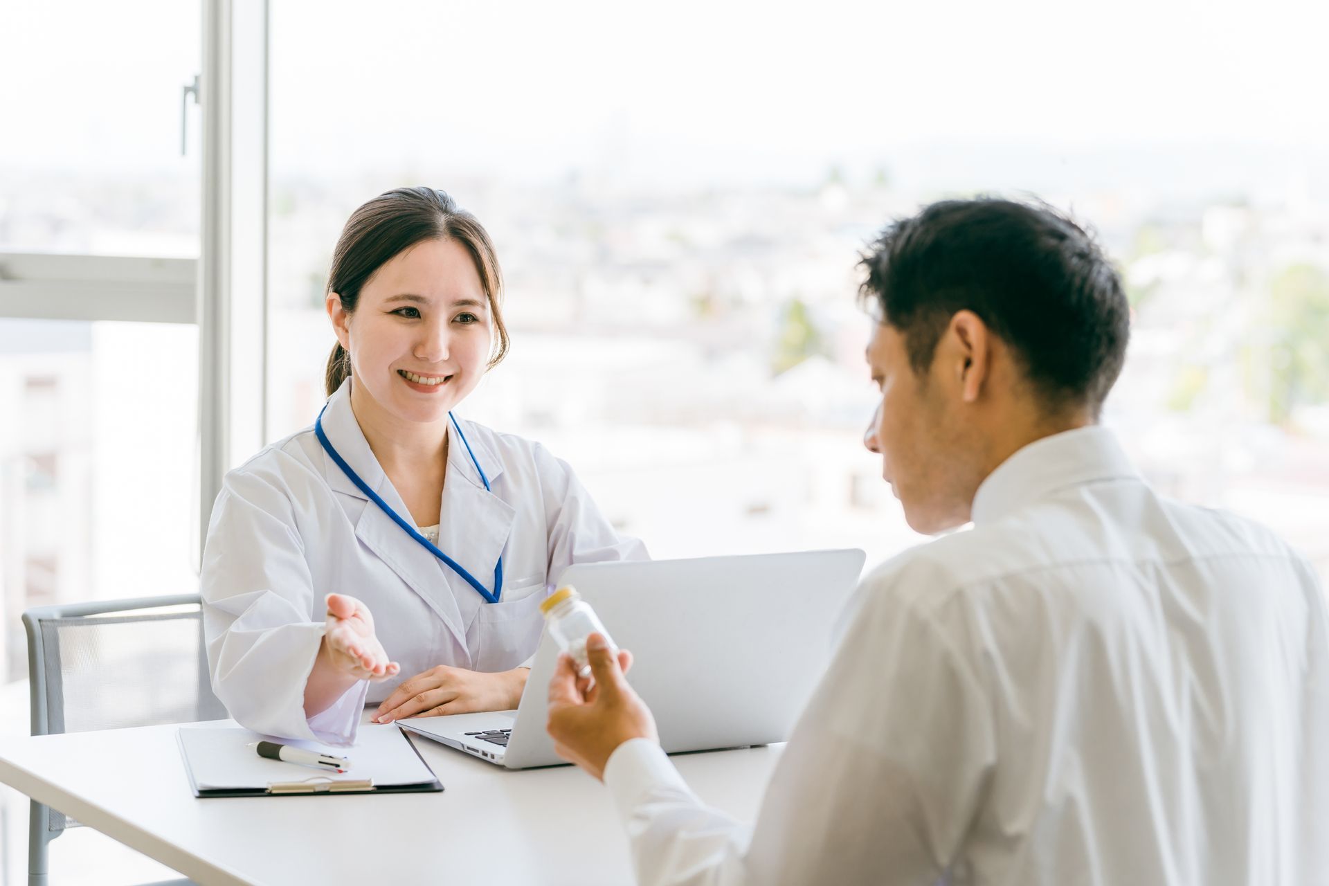 A doctor is talking to a patient who is sitting at a table with a laptop.