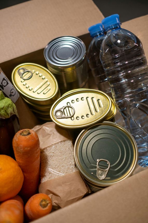 A cardboard box filled with canned food , fruits and vegetables.