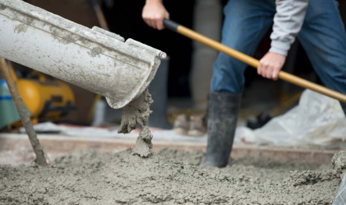 A man is pouring concrete into the ground with a shovel.