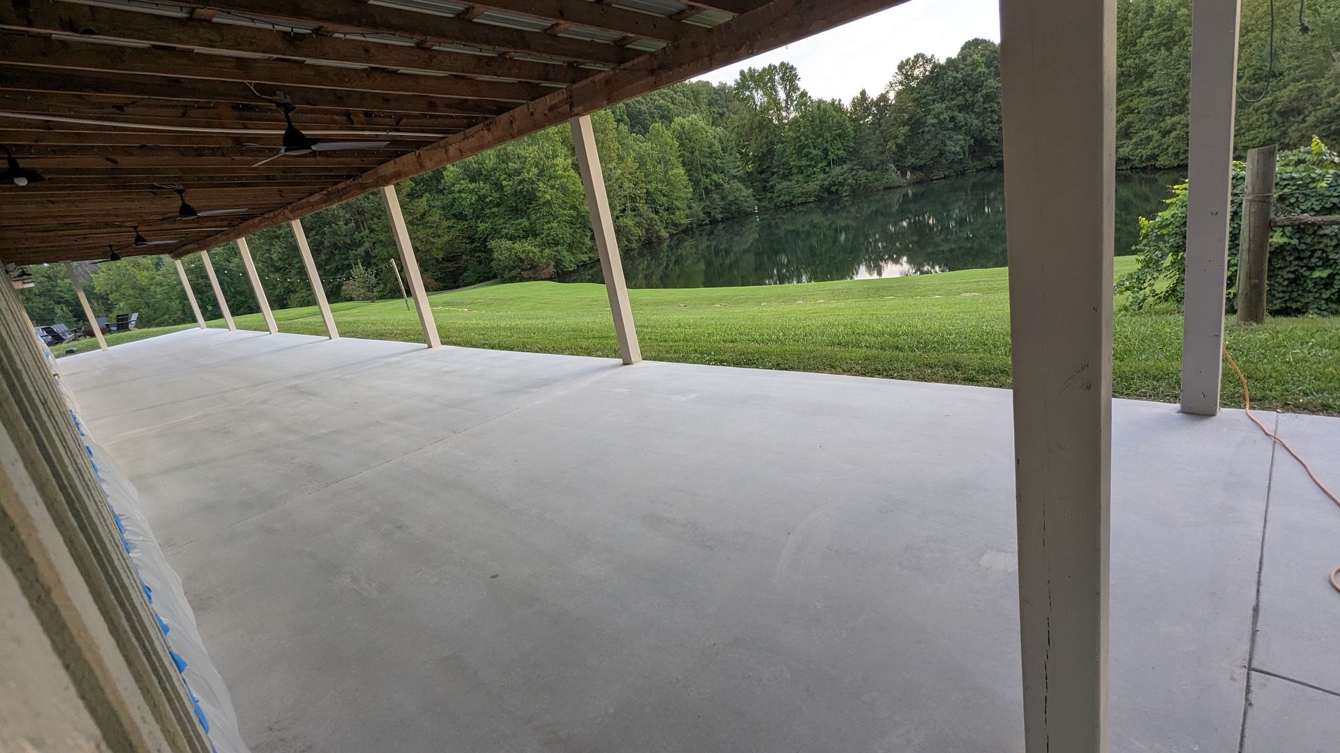 A large concrete patio under a wooden roof with a view of a golf course.