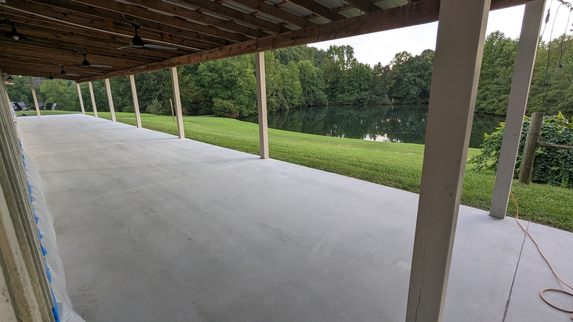 A large concrete patio with a wooden roof and a lake in the background.