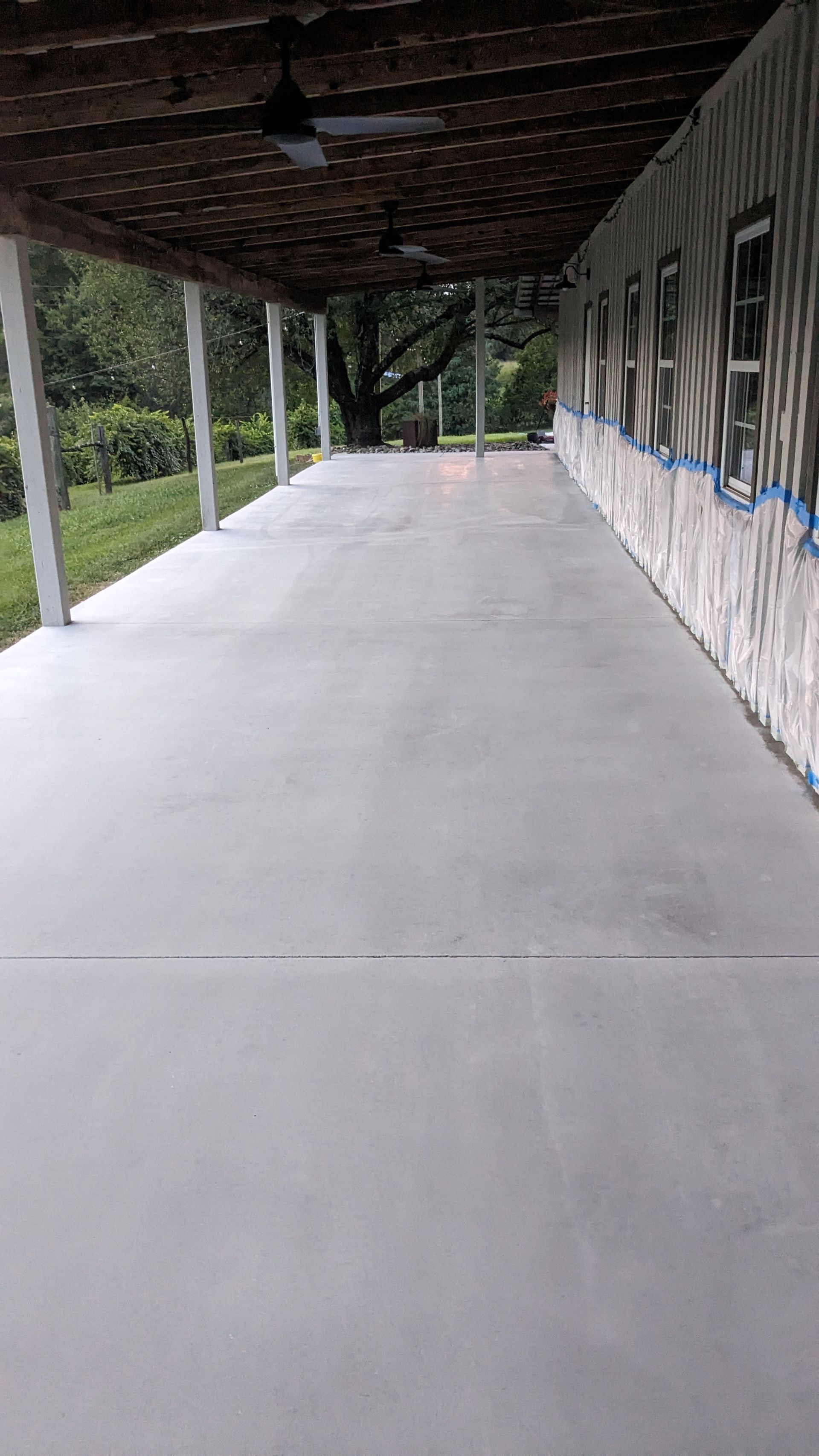 A long concrete porch with a wooden roof and a tree in the background.