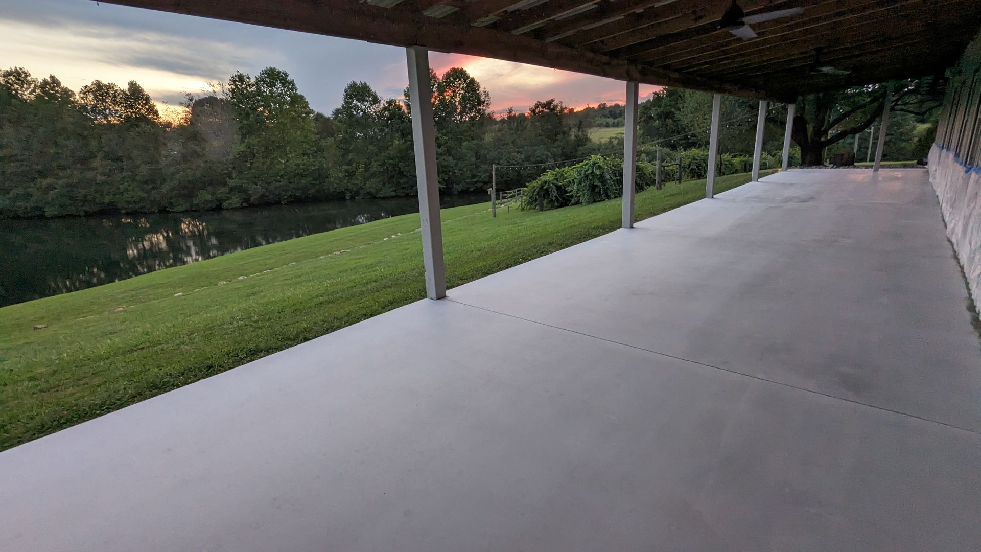 A covered walkway leading to a lake with a sunset in the background.