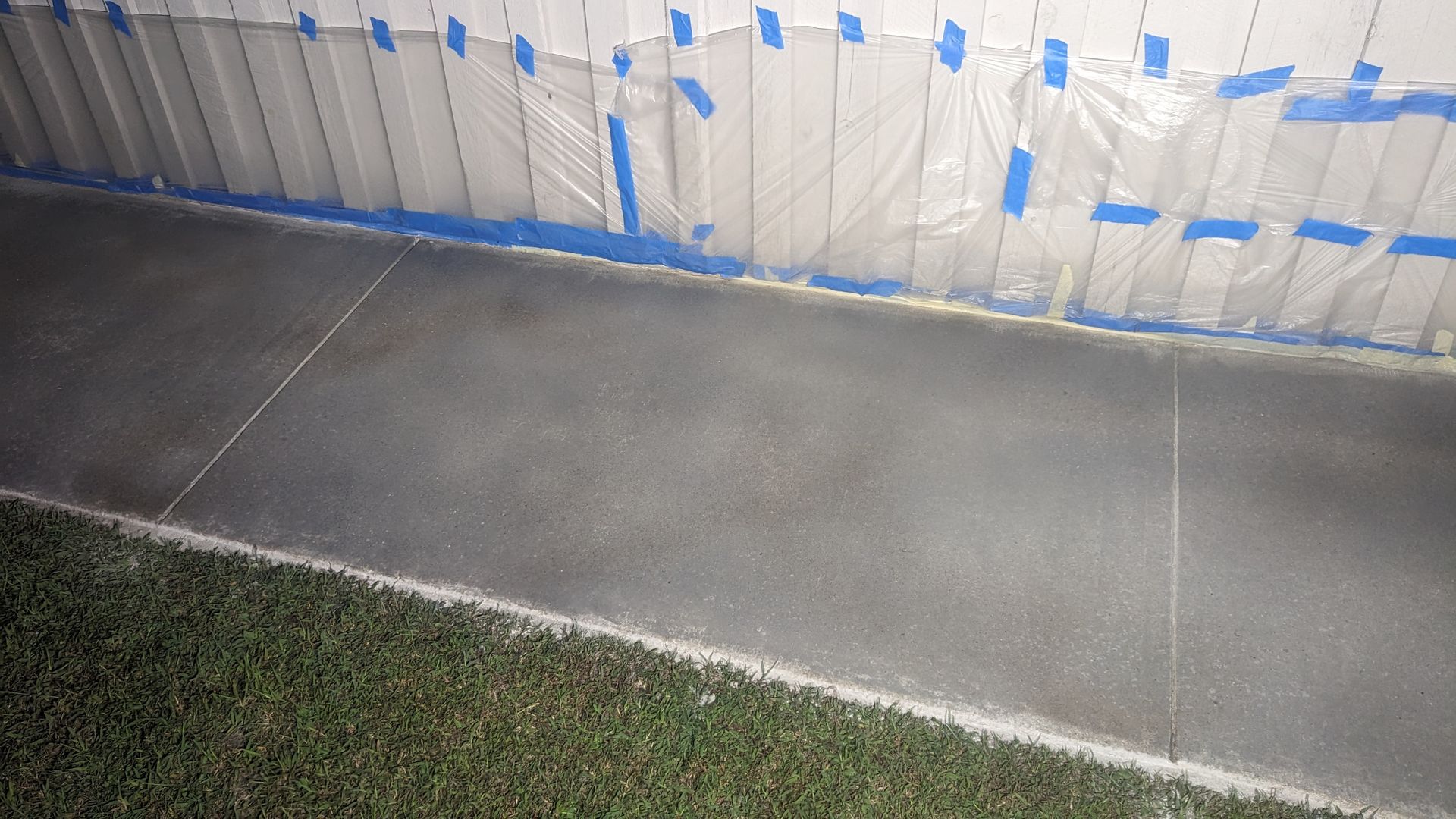 A concrete floor with blue tape on it is being painted.