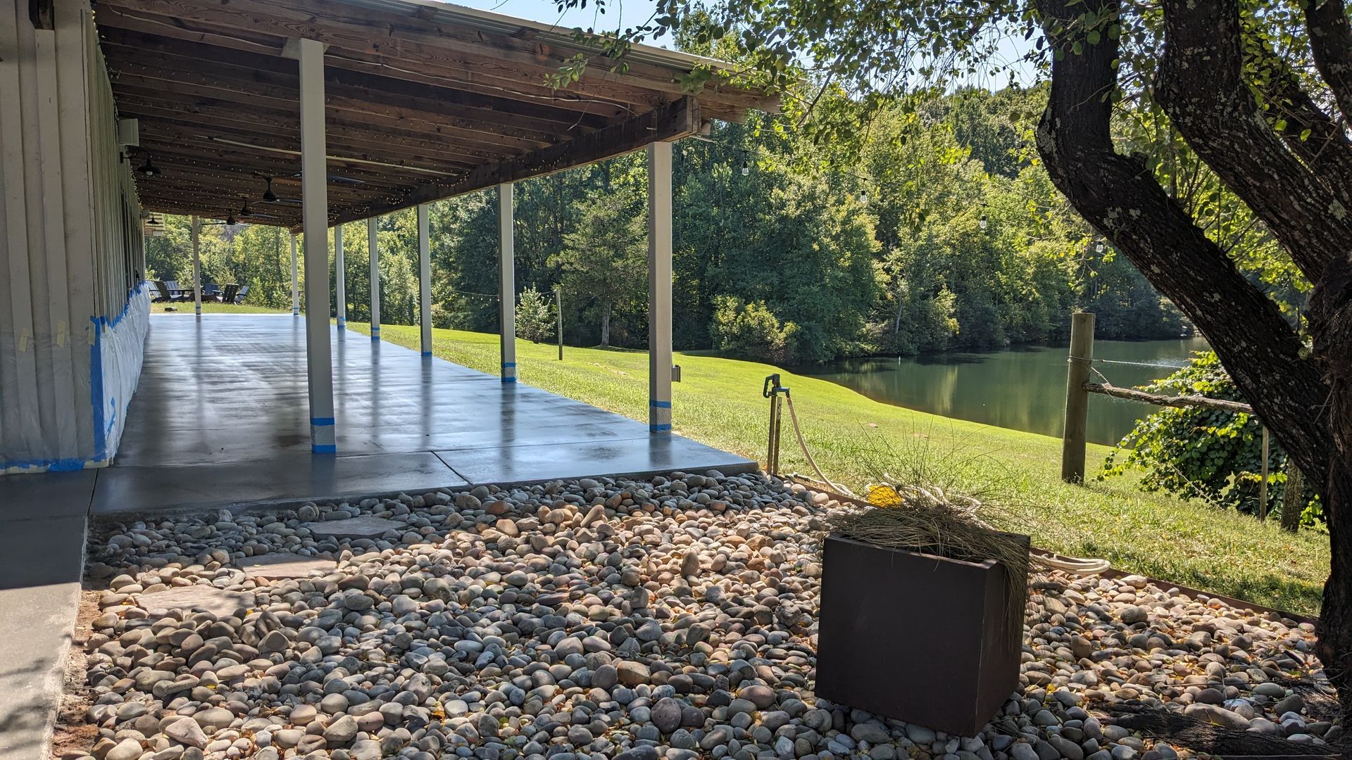 a large covered patio with a tree in the foreground and a lake in the background .
