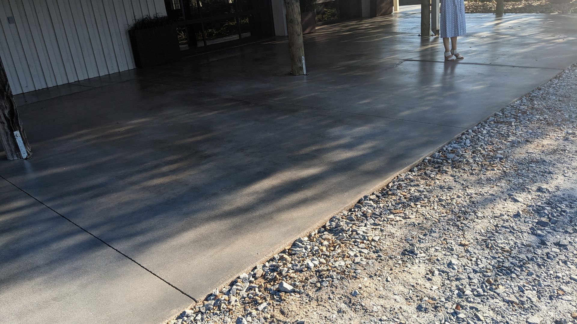 a person is standing on a concrete sidewalk next to a gravel road .