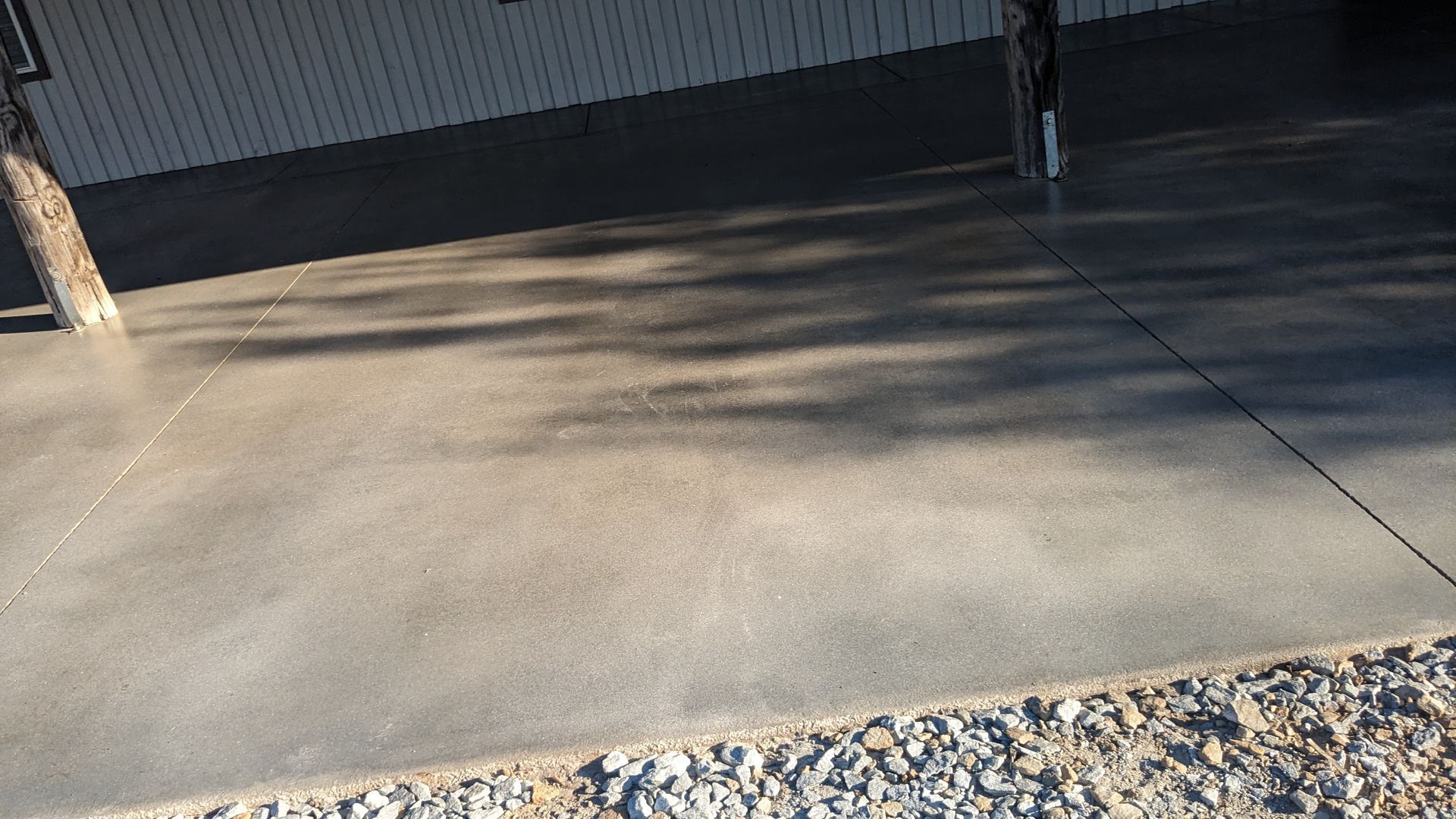 a concrete driveway with gravel and a tree in the background .
