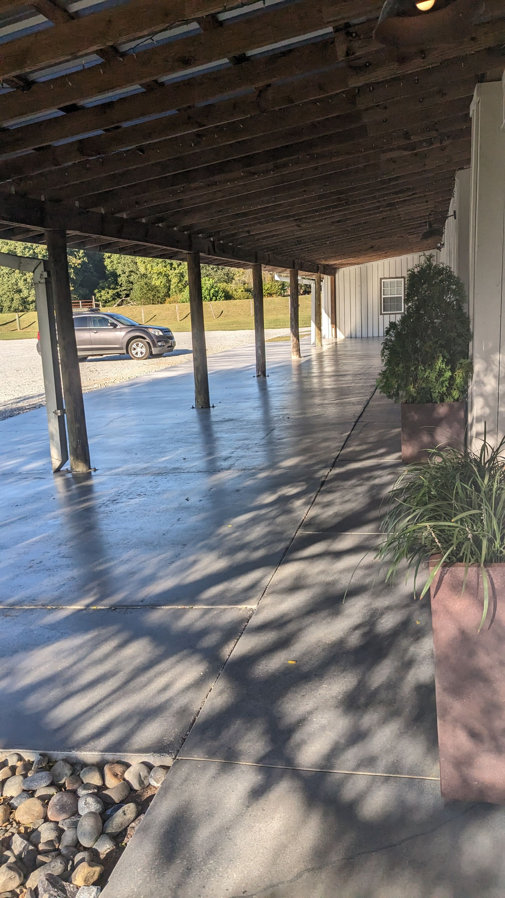 a long concrete walkway under a wooden roof with a car parked in the background .