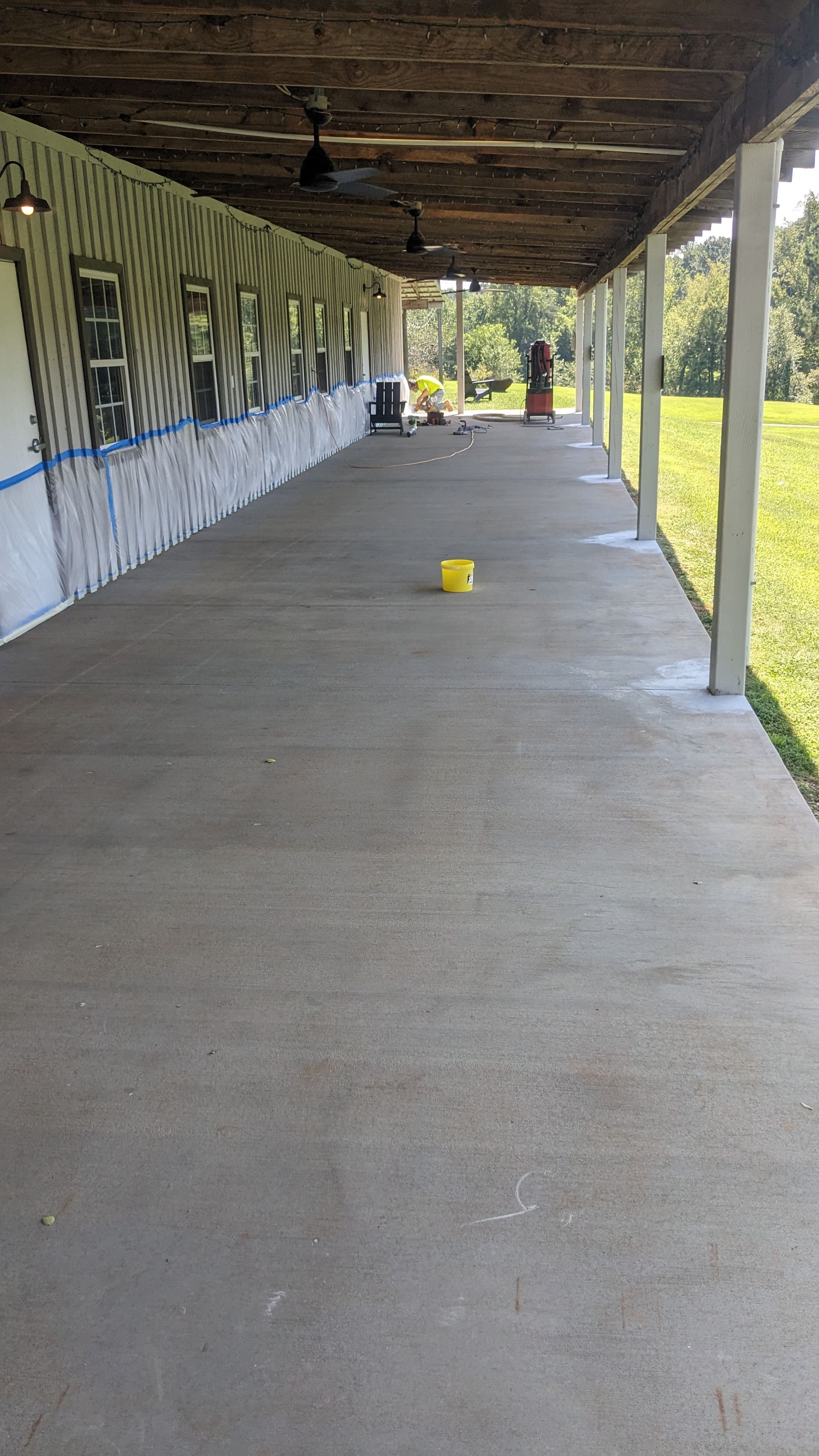 A long concrete porch with a yellow bucket in the middle of it.