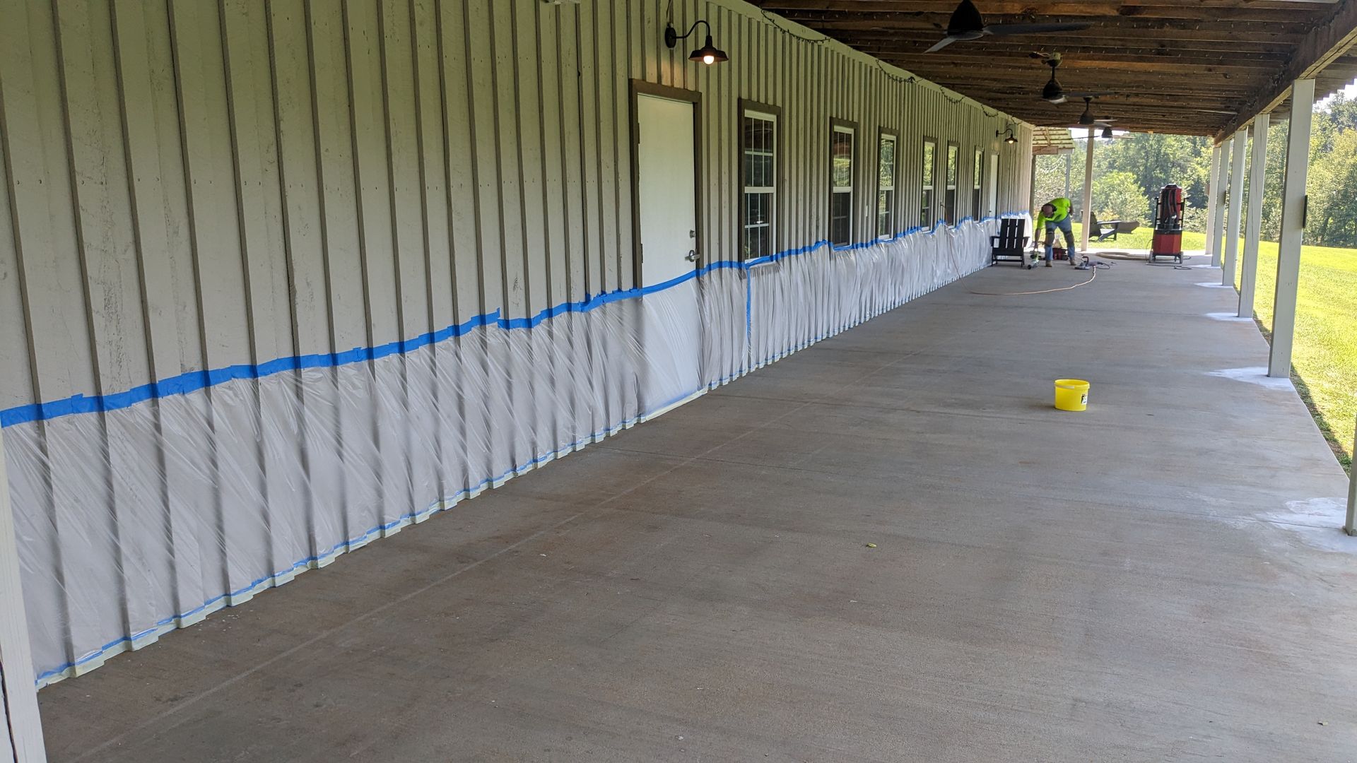 A long covered porch with a yellow bucket on the floor.