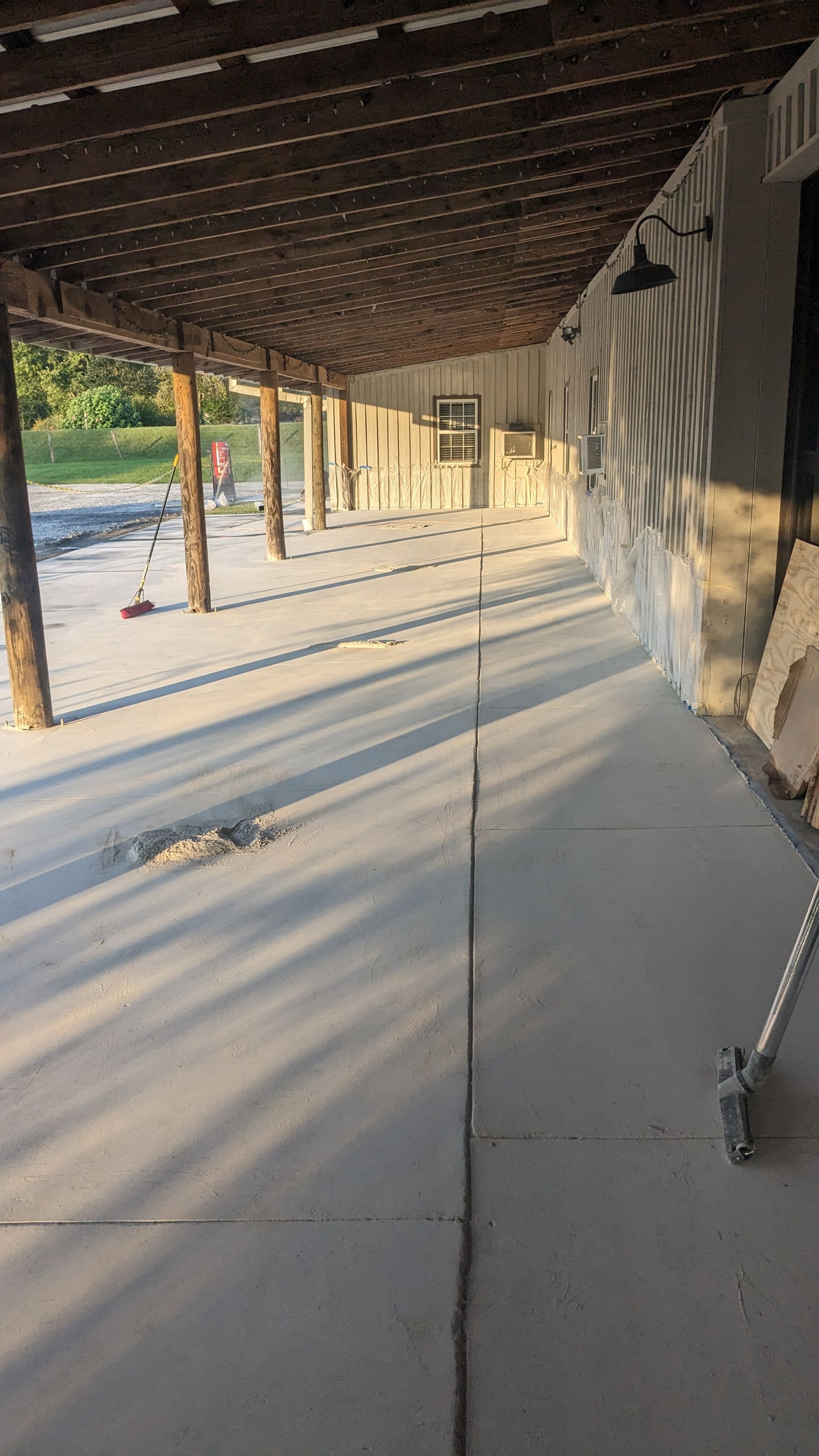 A concrete walkway under a covered porch with a broom in the foreground.