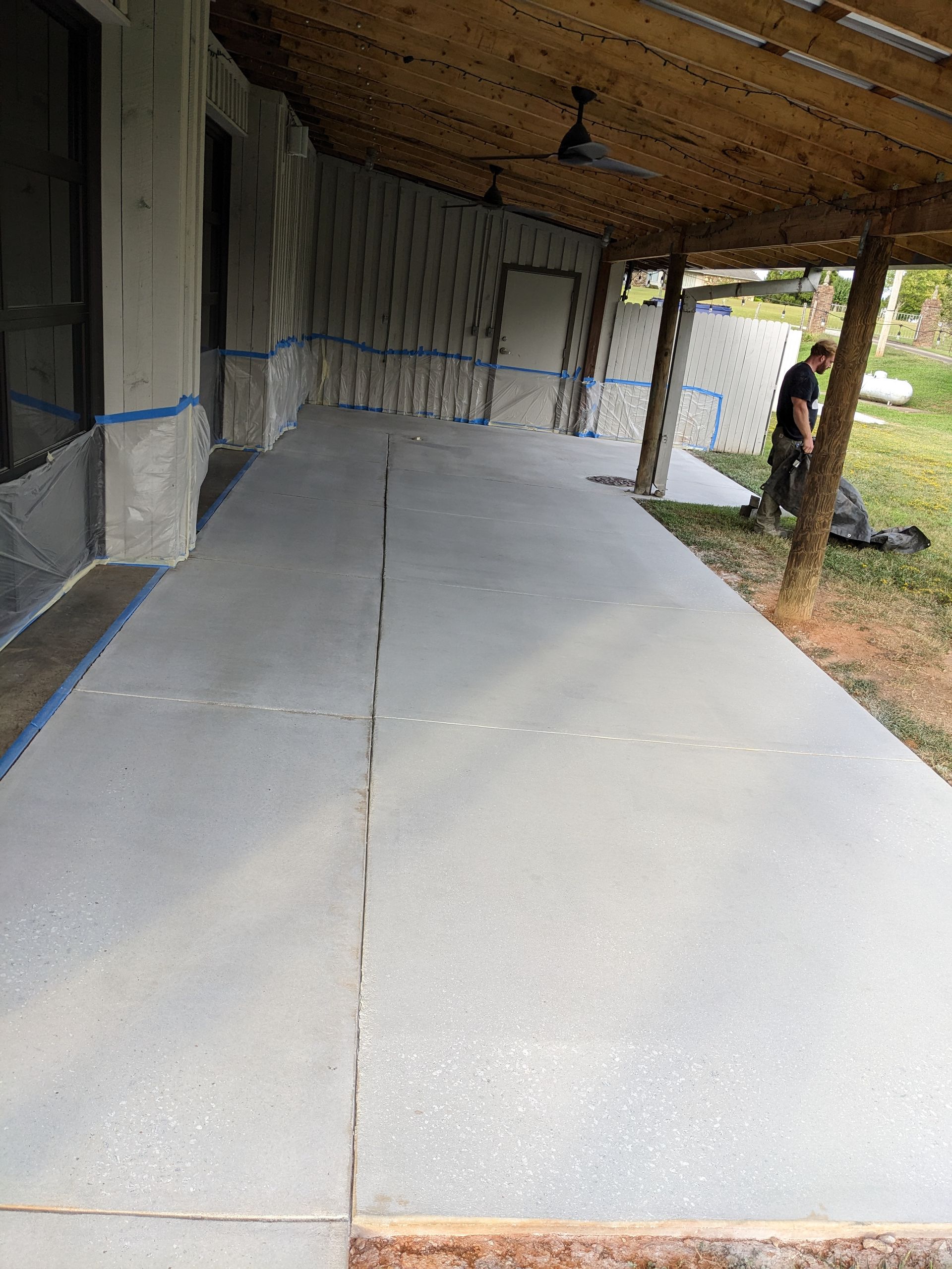 A man is standing on a concrete porch under a wooden roof.