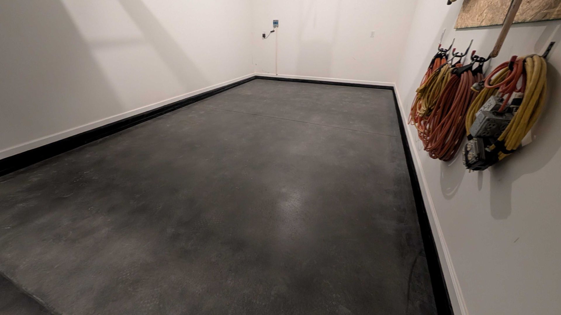 A room with a concrete floor and a bunch of wires hanging on the wall.