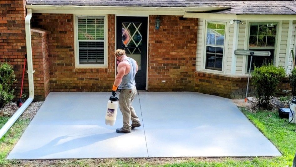 A man is standing on a concrete driveway in front of a brick house.