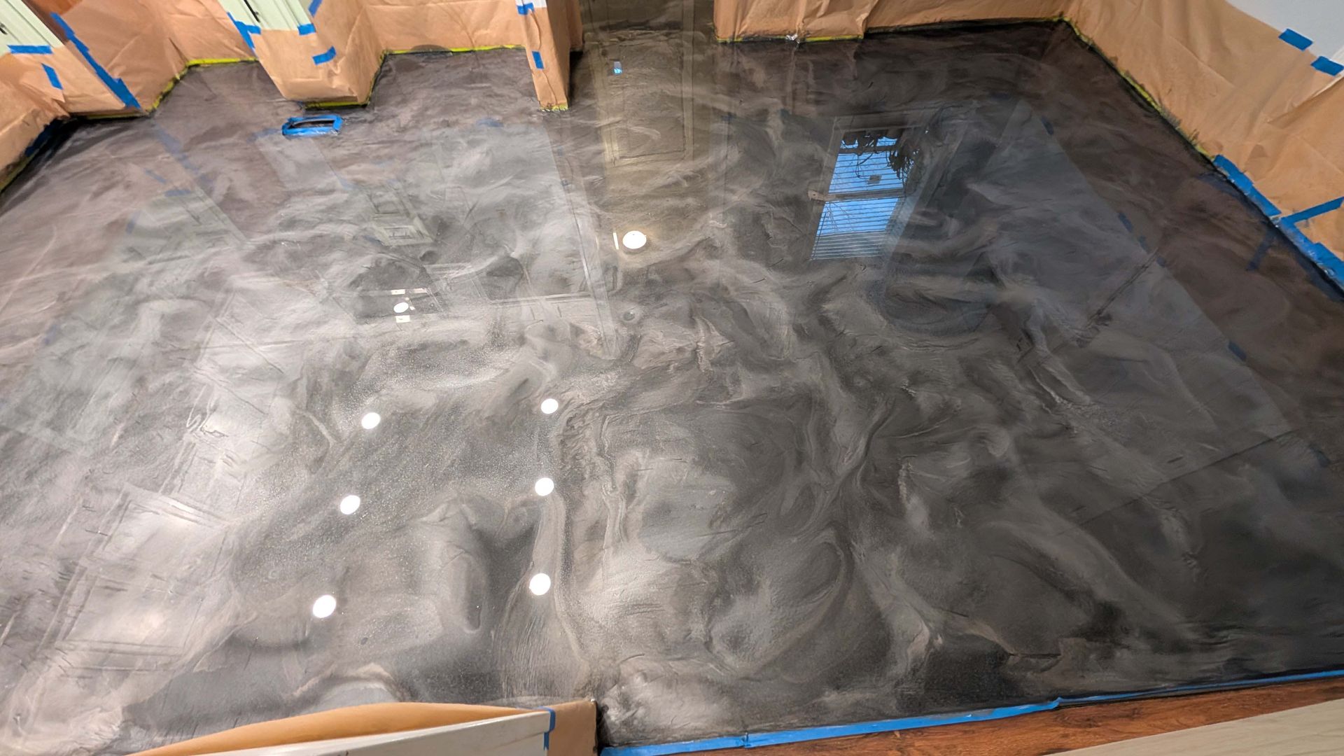 Freshly finished metallic epoxy floor in a residential room with swirled patterns and protective tap