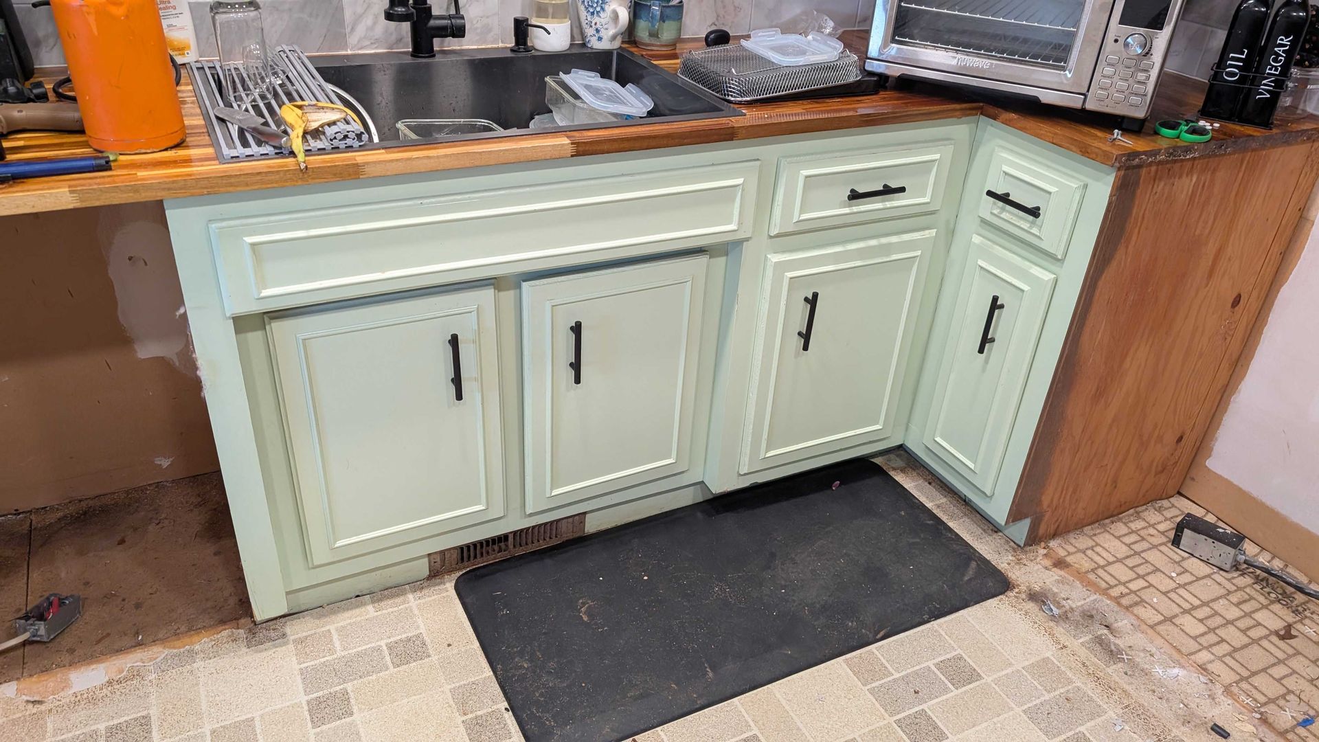 A kitchen with green cabinets , a sink , and a toaster oven.