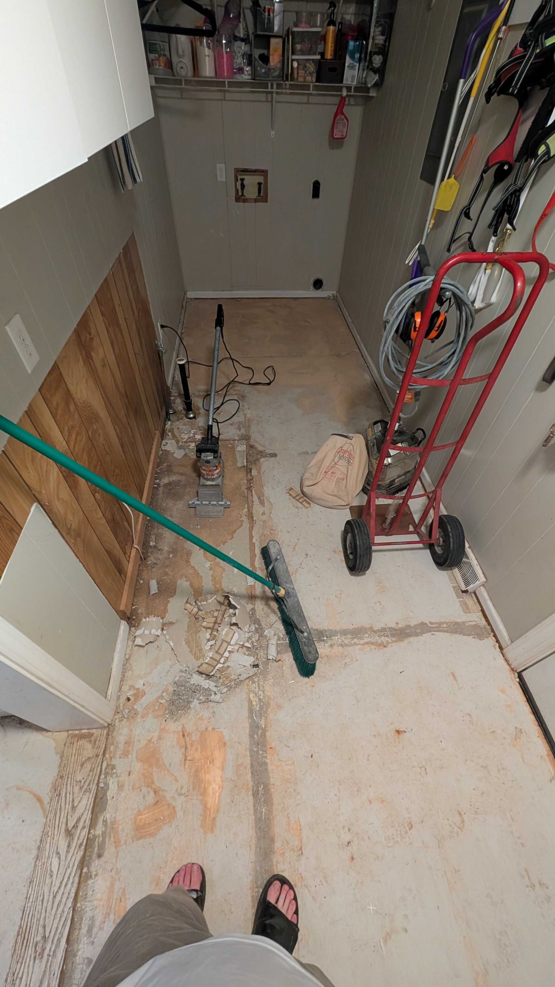 A person is standing in a hallway with a broom and a dolly.