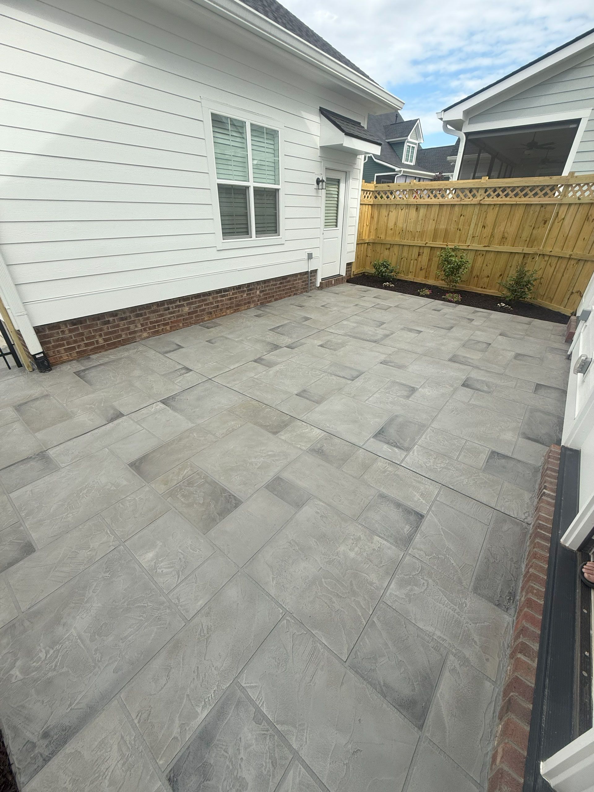 Decorative concrete patio with gray stamped overlay finish beside a white house in Greenville,SC.