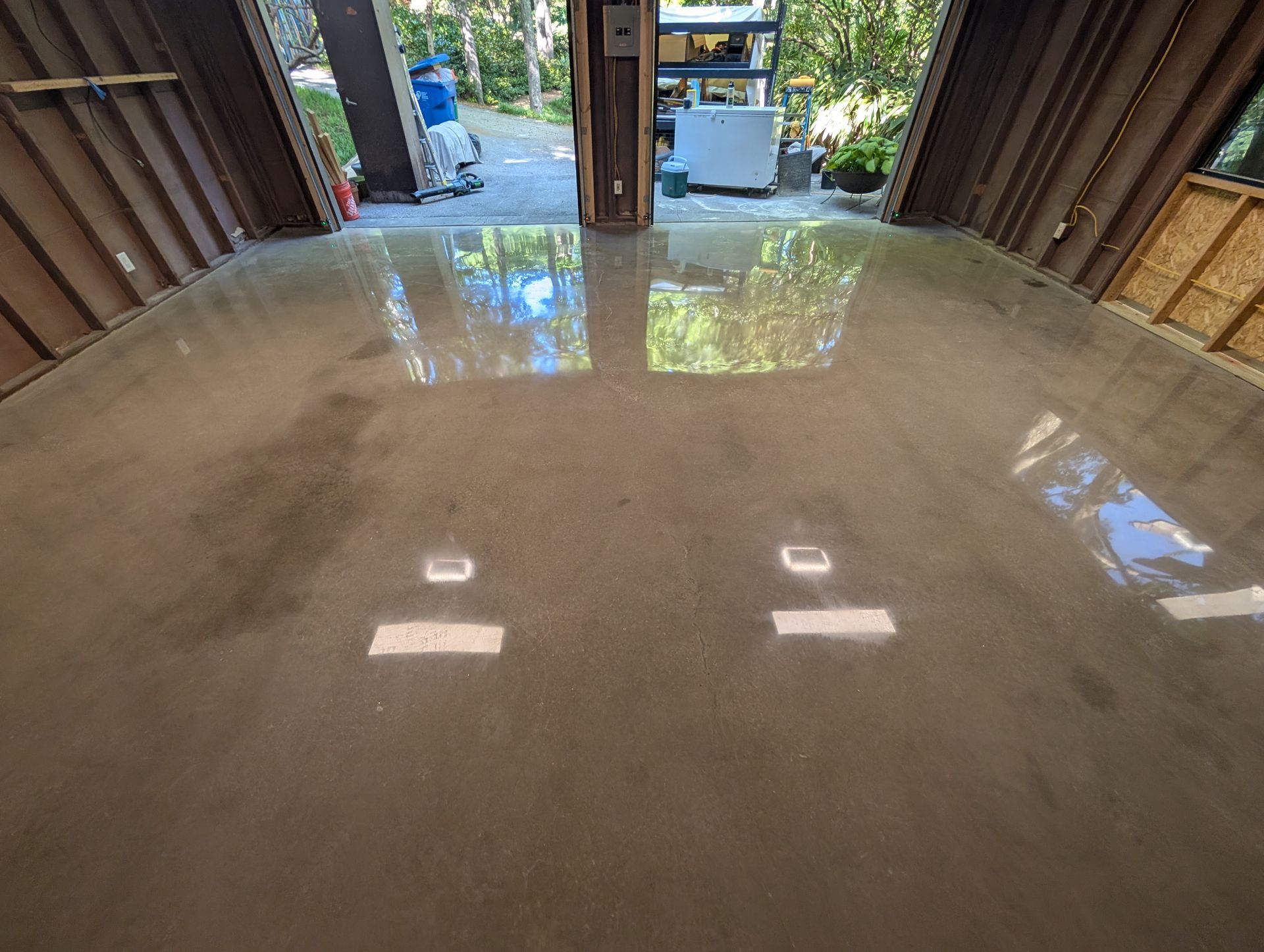 Shiny concrete garage floor with reflections, open doors, and outdoor light beyond.