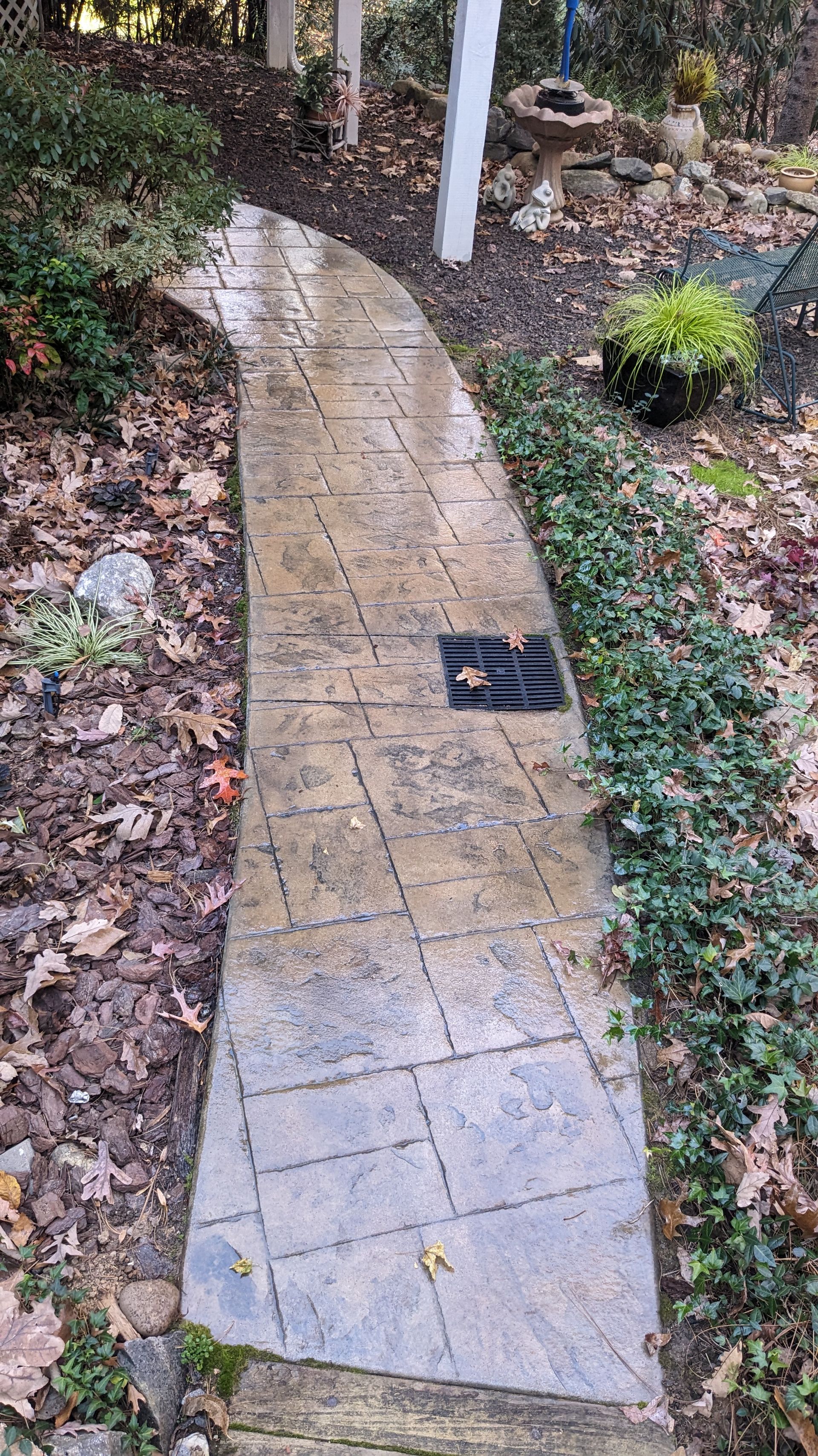A stone walkway in a garden with a drain on the side.