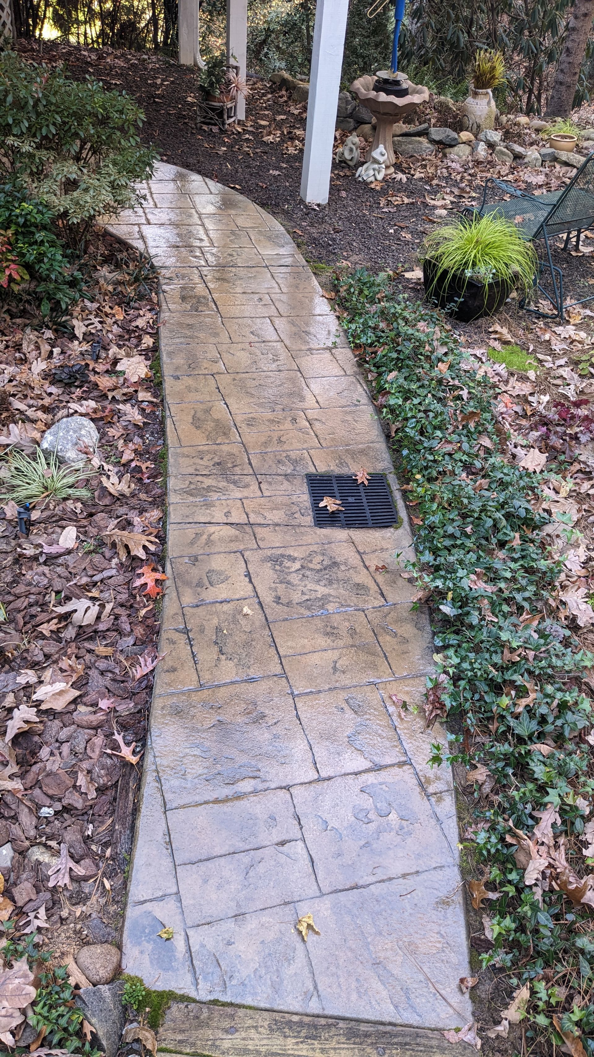 A walkway in a garden with a drain on the side of it.