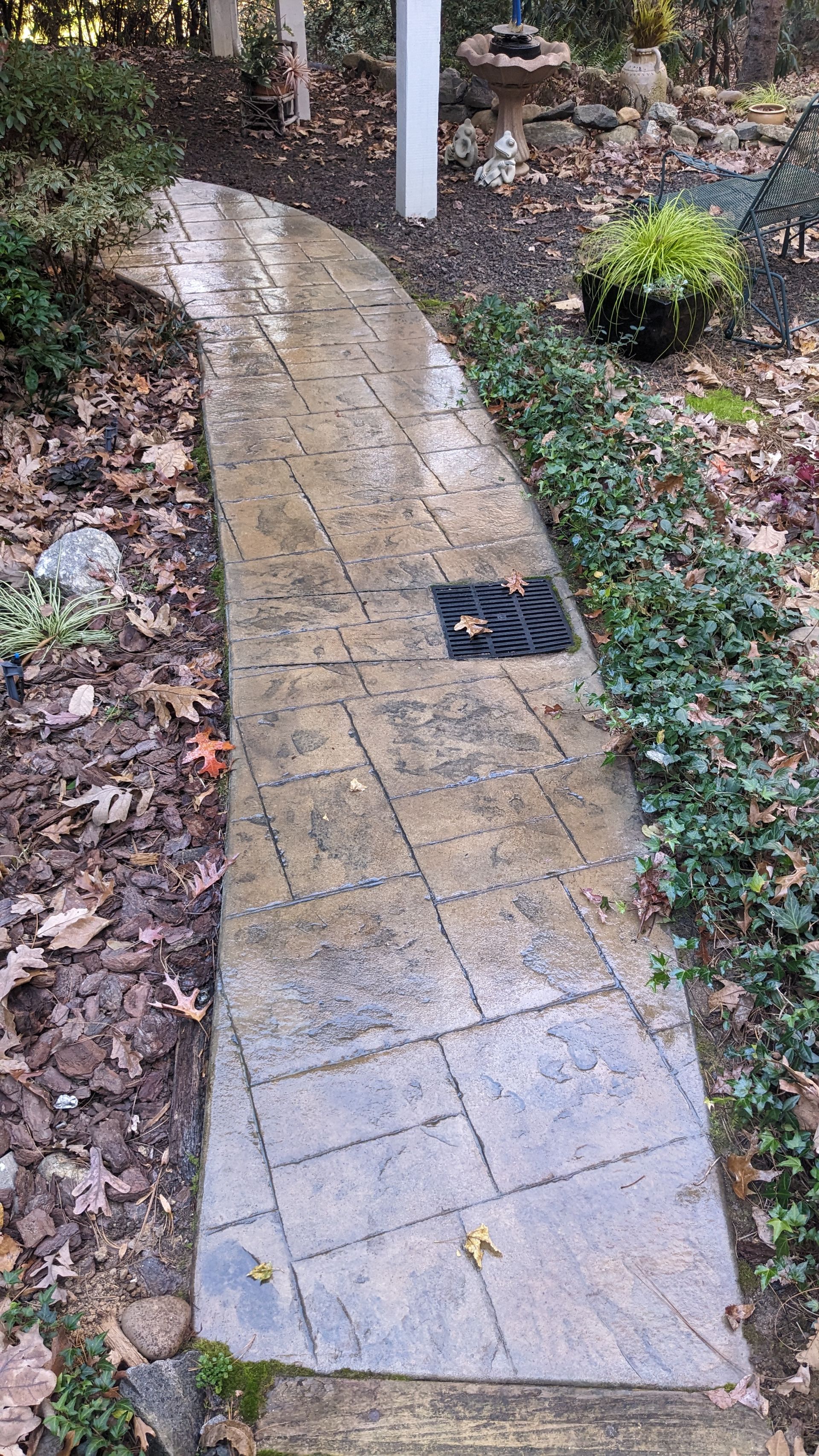 A concrete walkway leading to a bird bath in a garden.