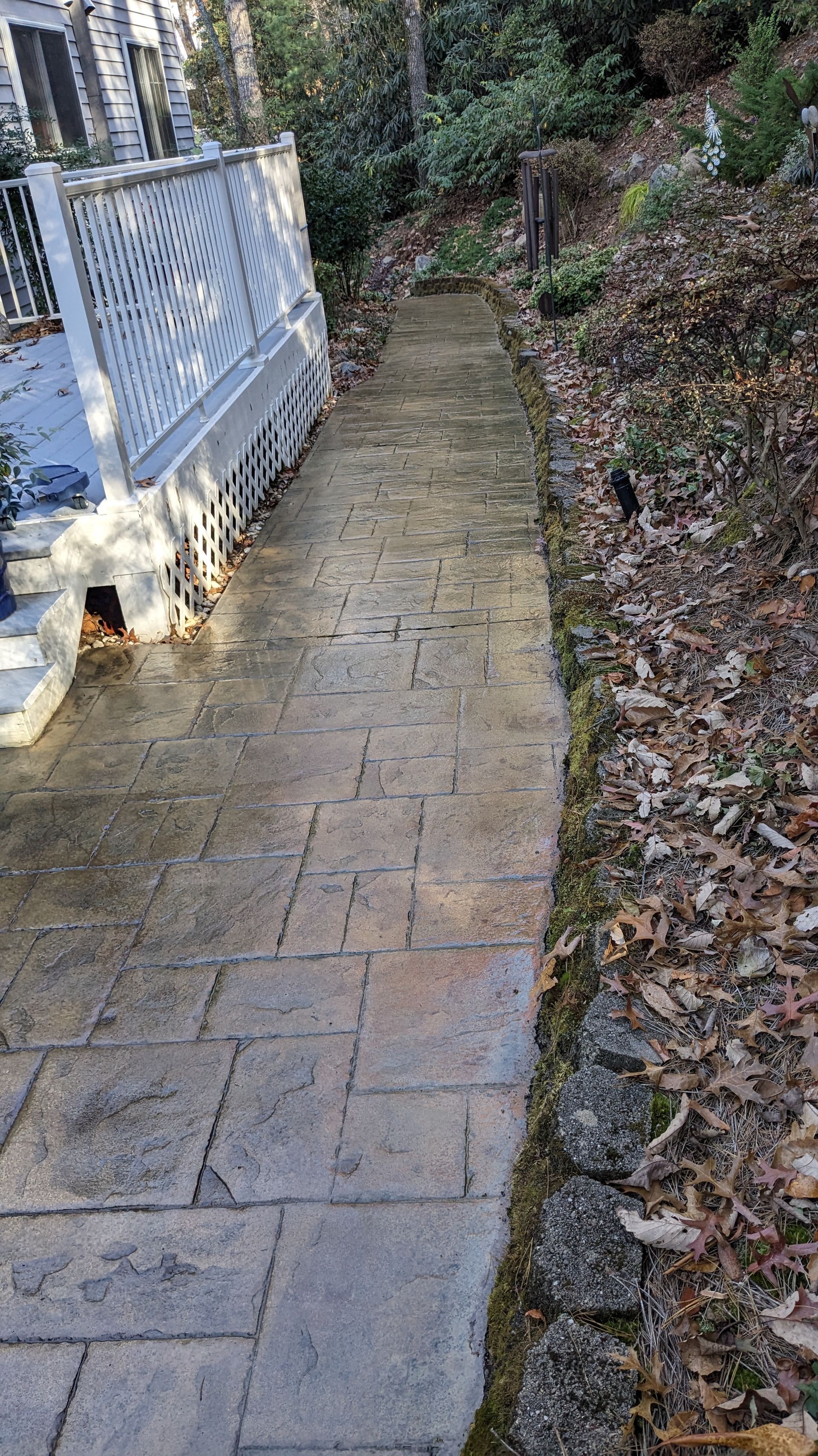 A brick walkway leading to a house with leaves on the ground.
