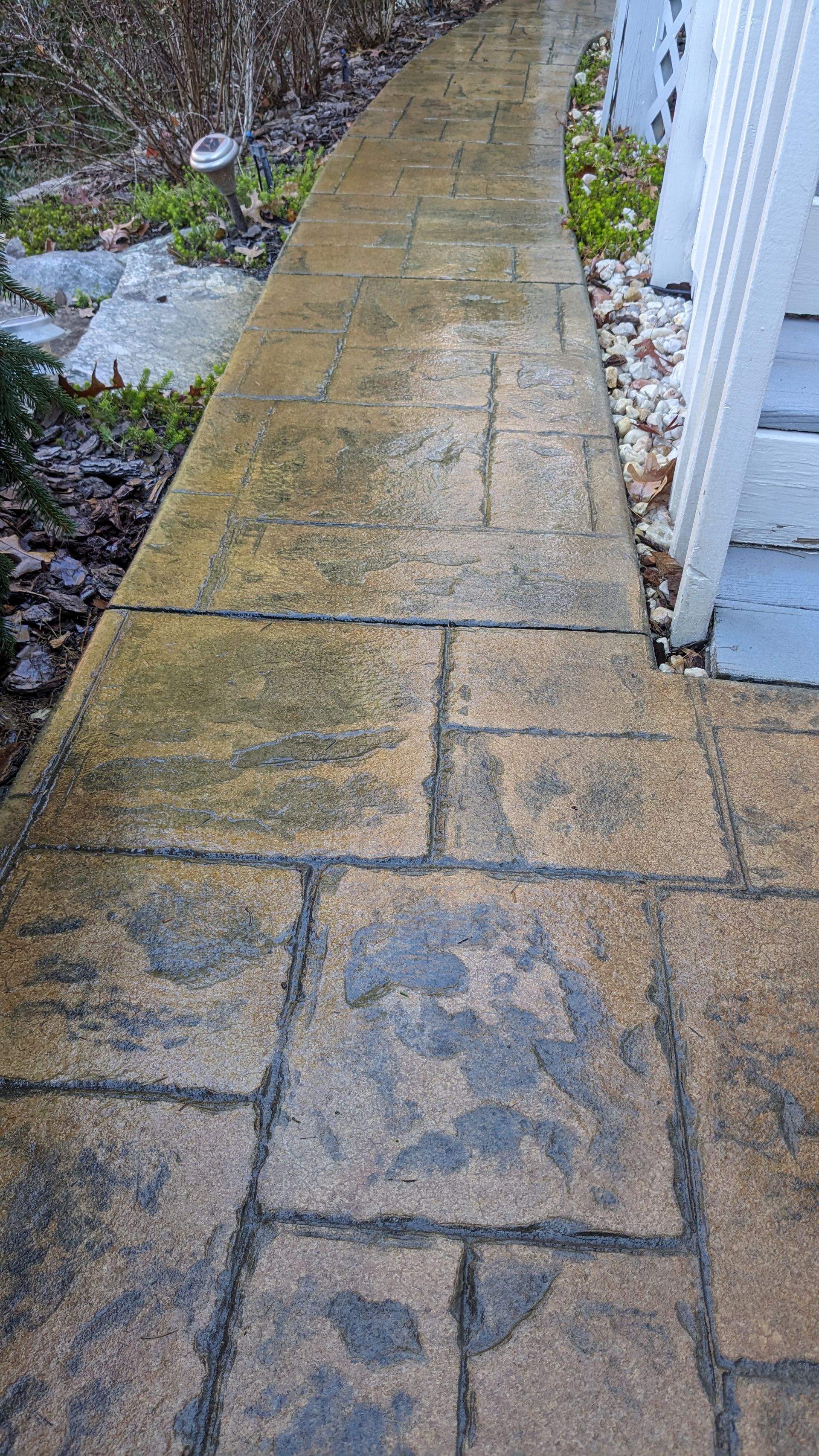 A dirty sidewalk next to a house with a white fence.