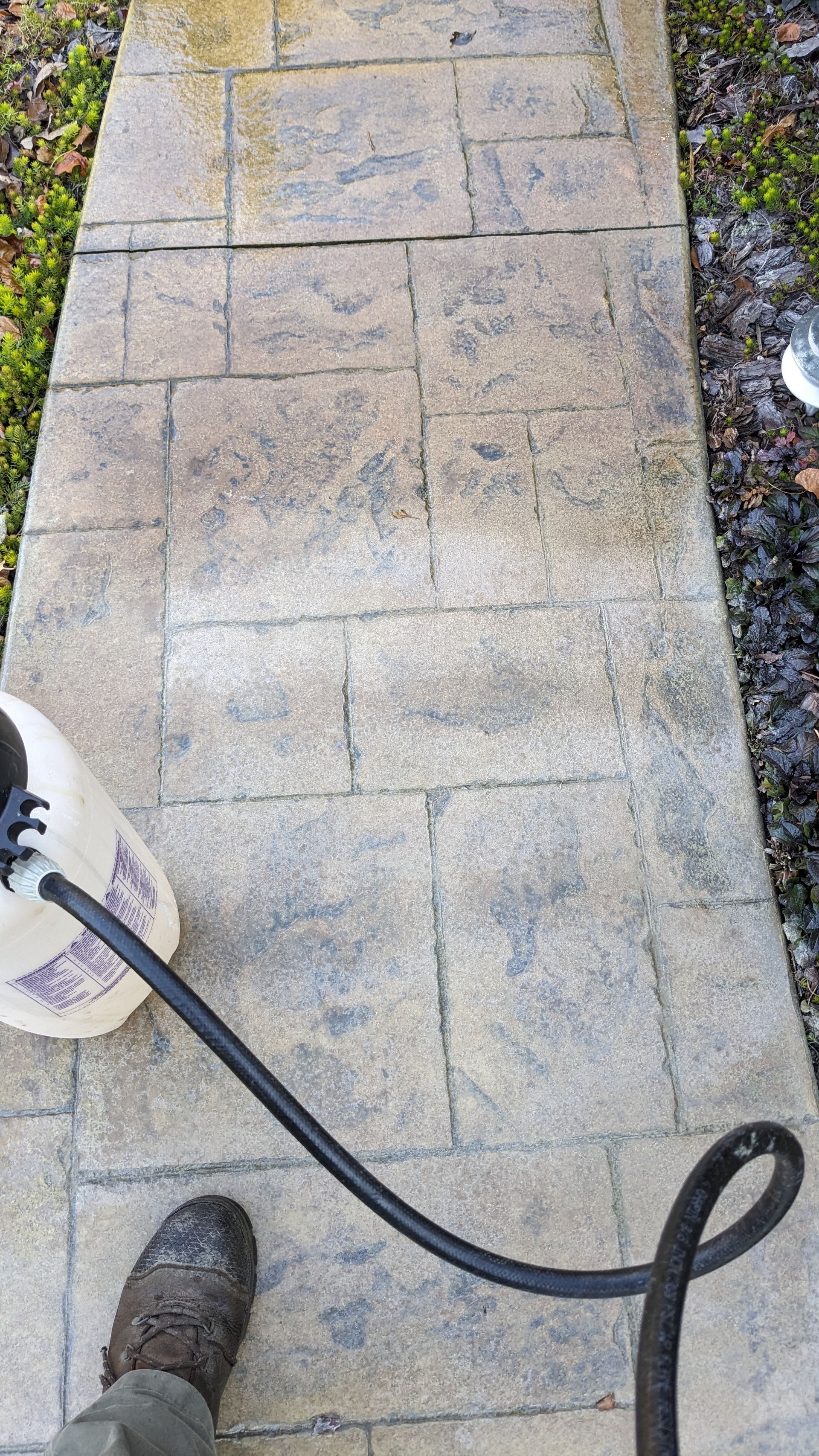 A person is cleaning a sidewalk with a pressure washer.