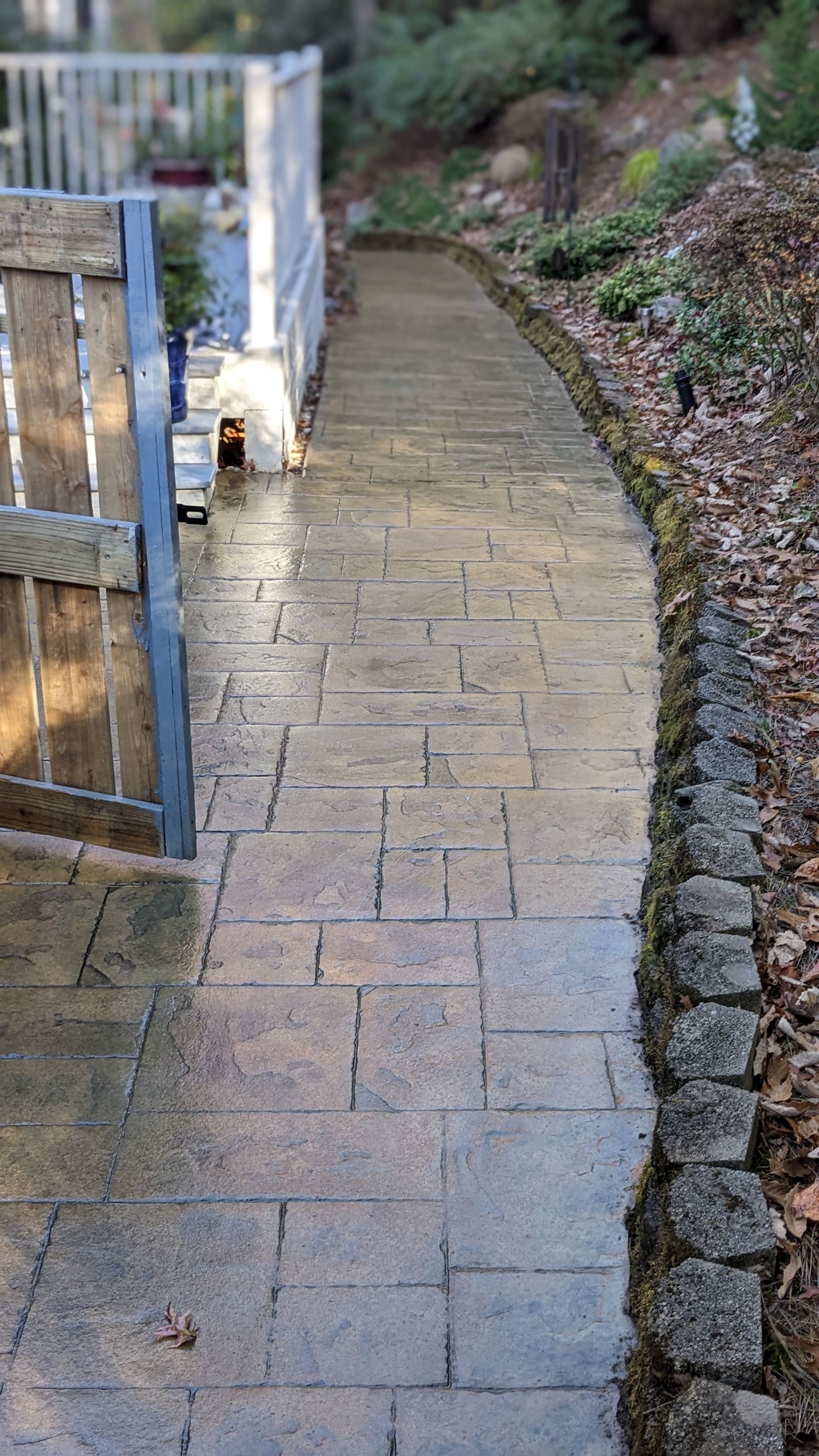 A brick walkway leading to a fence in a garden.