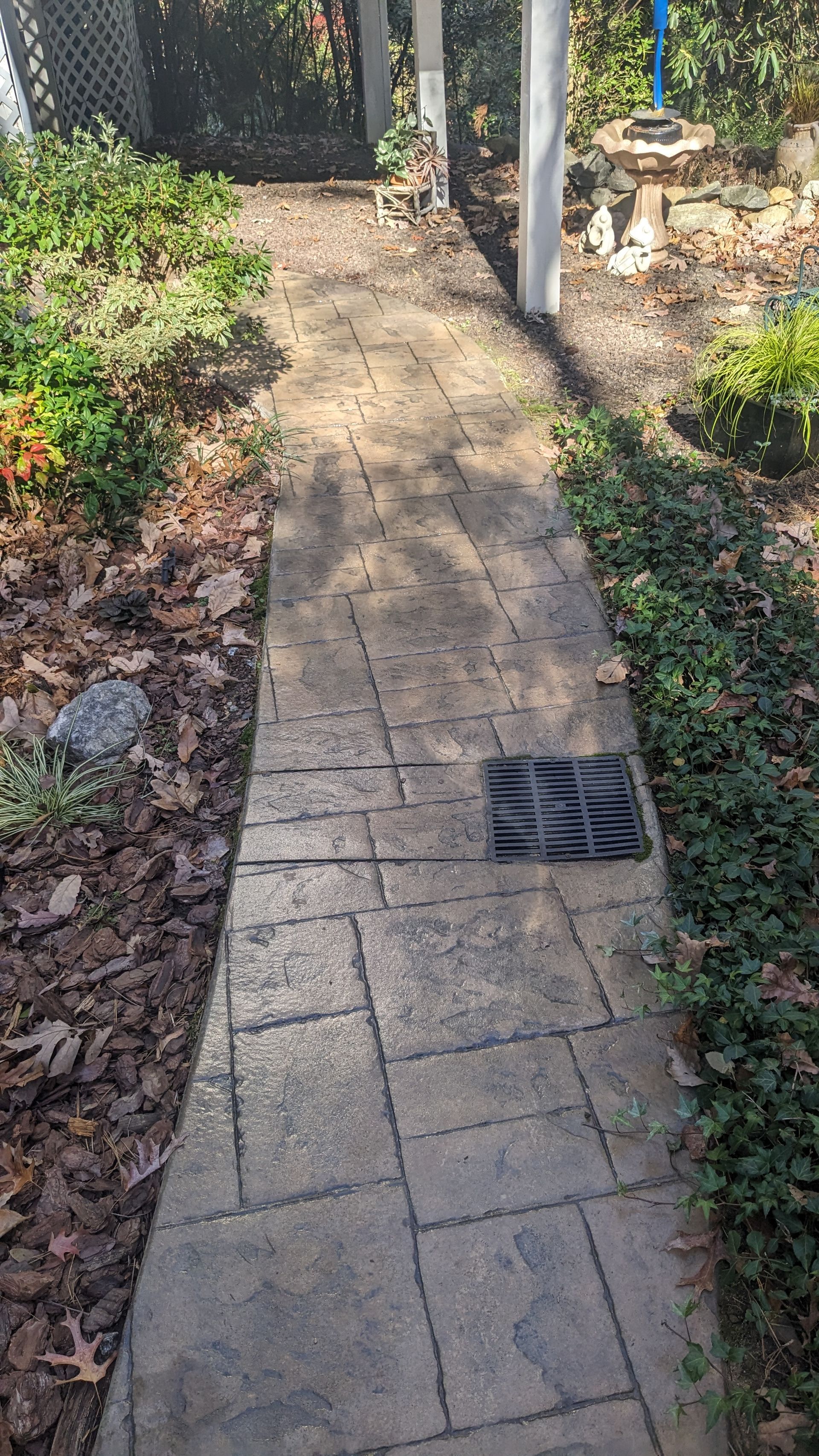 A brick walkway leading to a bird bath in a garden.