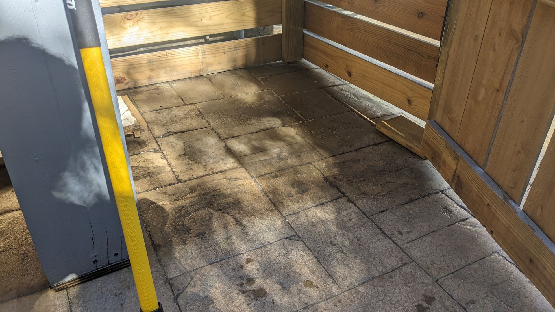 A yellow level is sitting on a tiled floor next to a wooden fence.