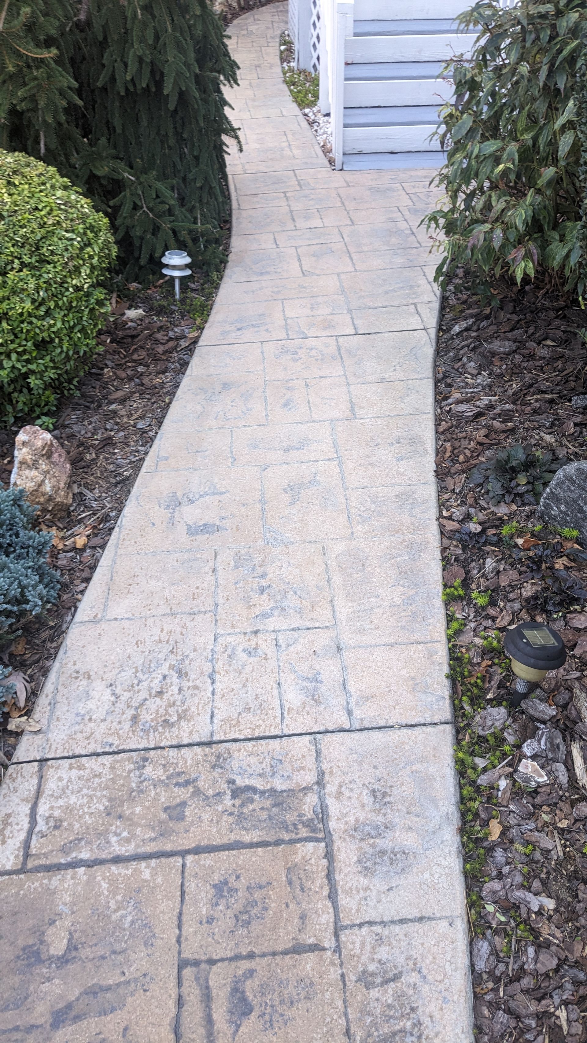 A brick walkway leading to a house with stairs in the background.
