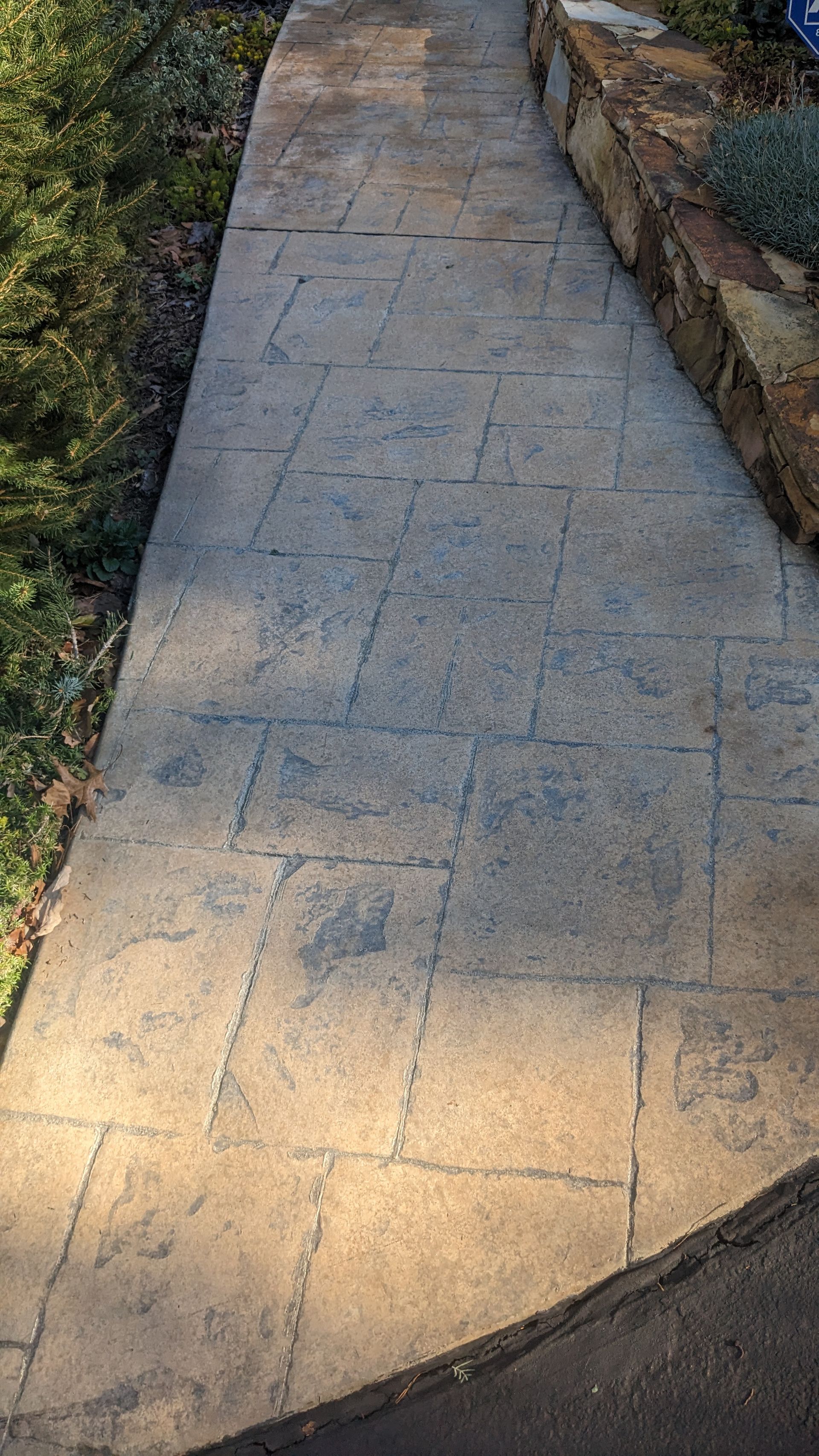 A concrete walkway leading to a stone wall.