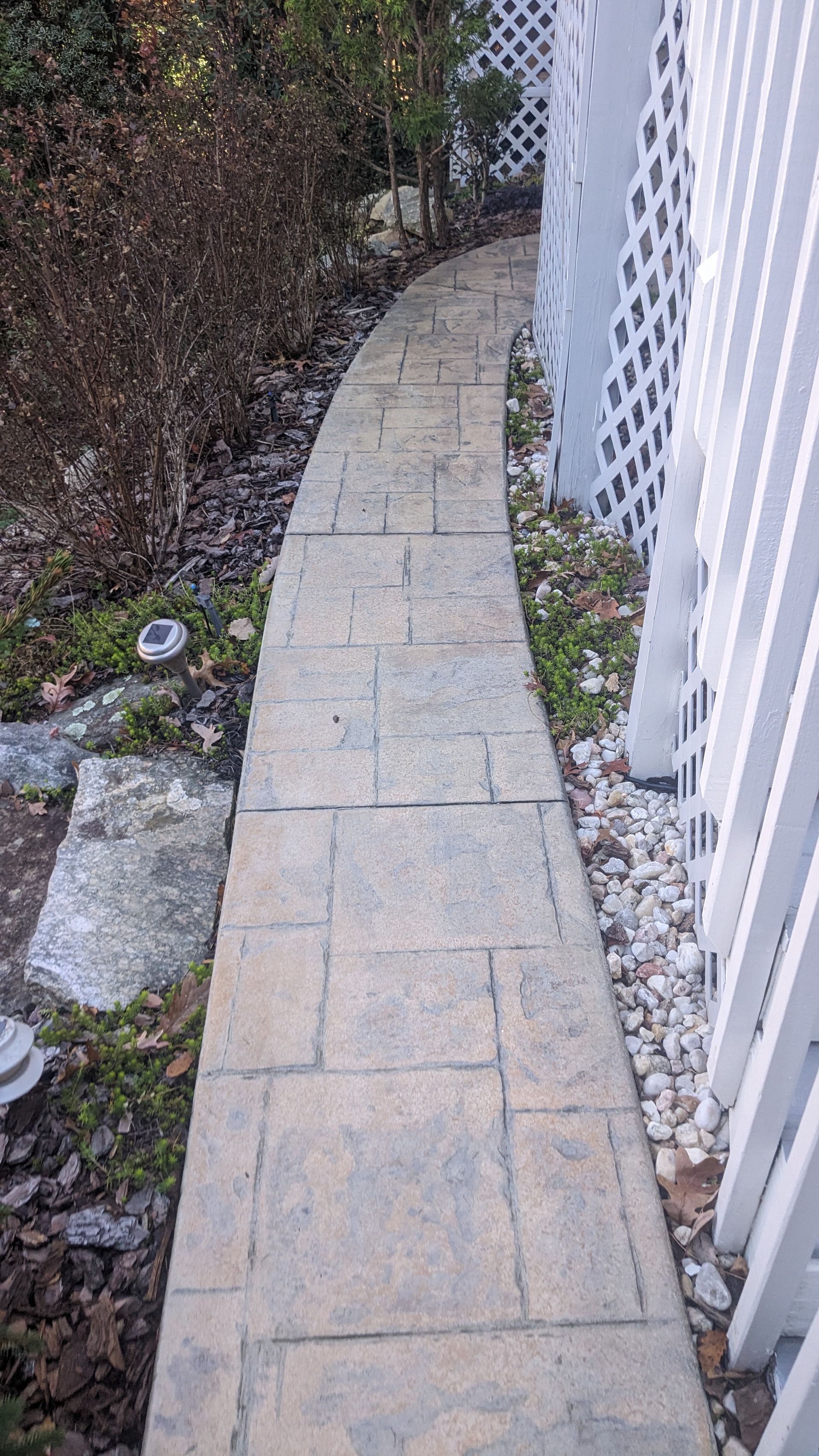 A brick walkway leading to a white fence.