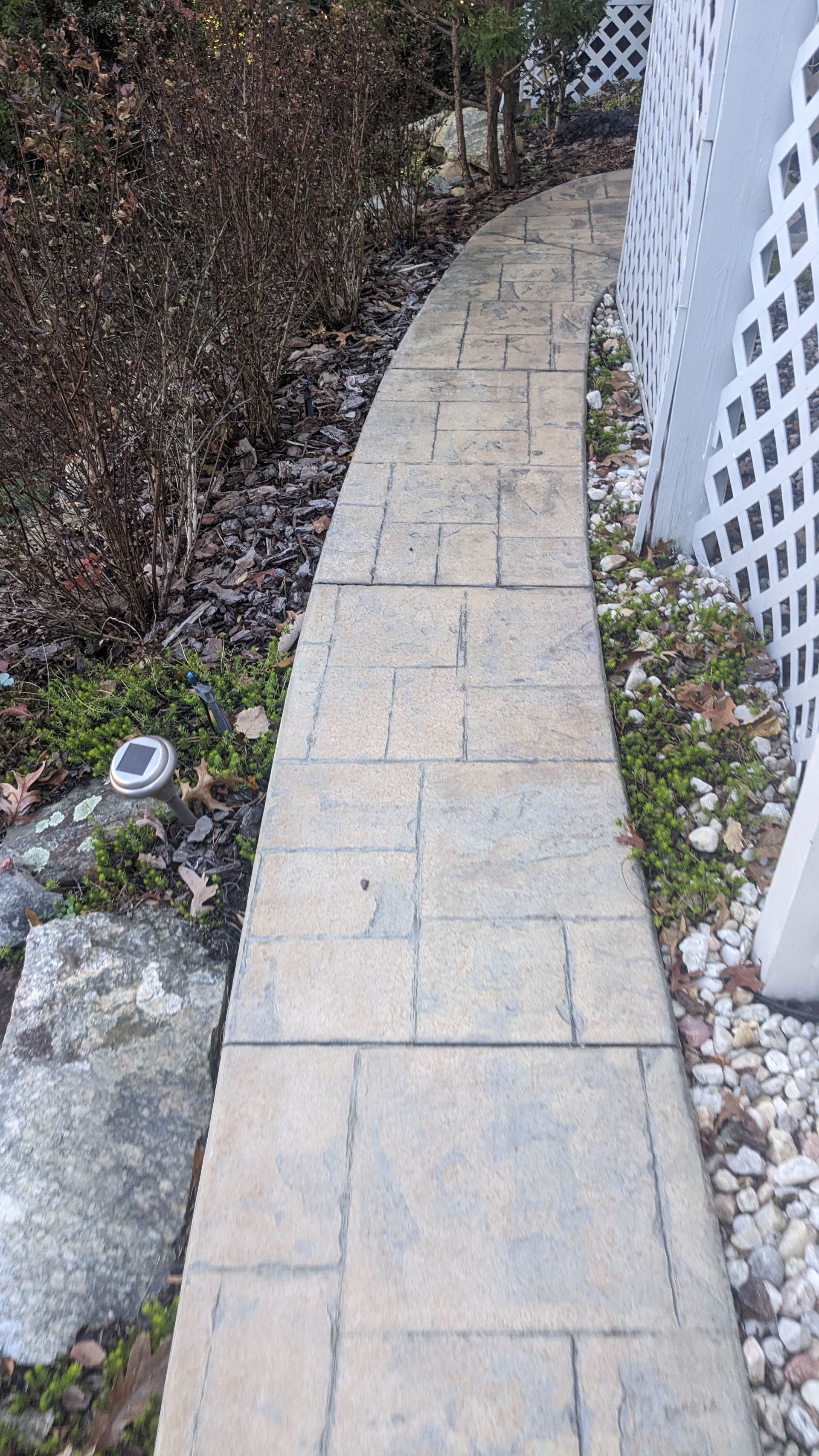 A stone walkway leading to a house with a white fence in the background.
