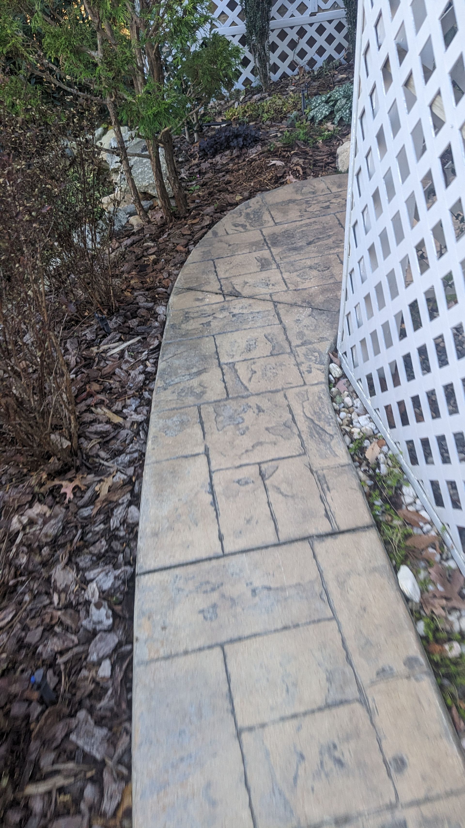A brick walkway leading to a fence in a backyard.