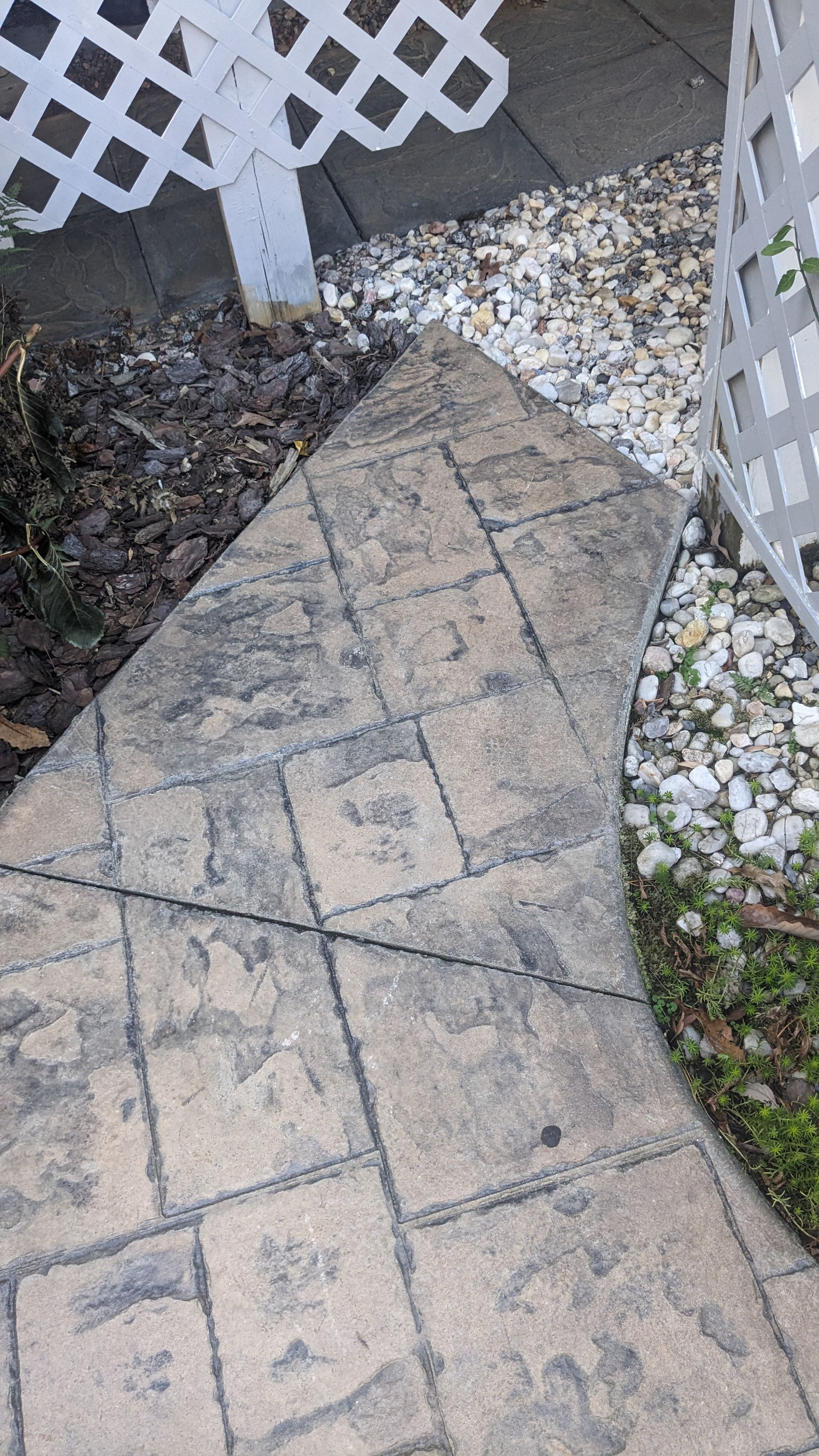 A brick walkway with a white lattice fence in the background.
