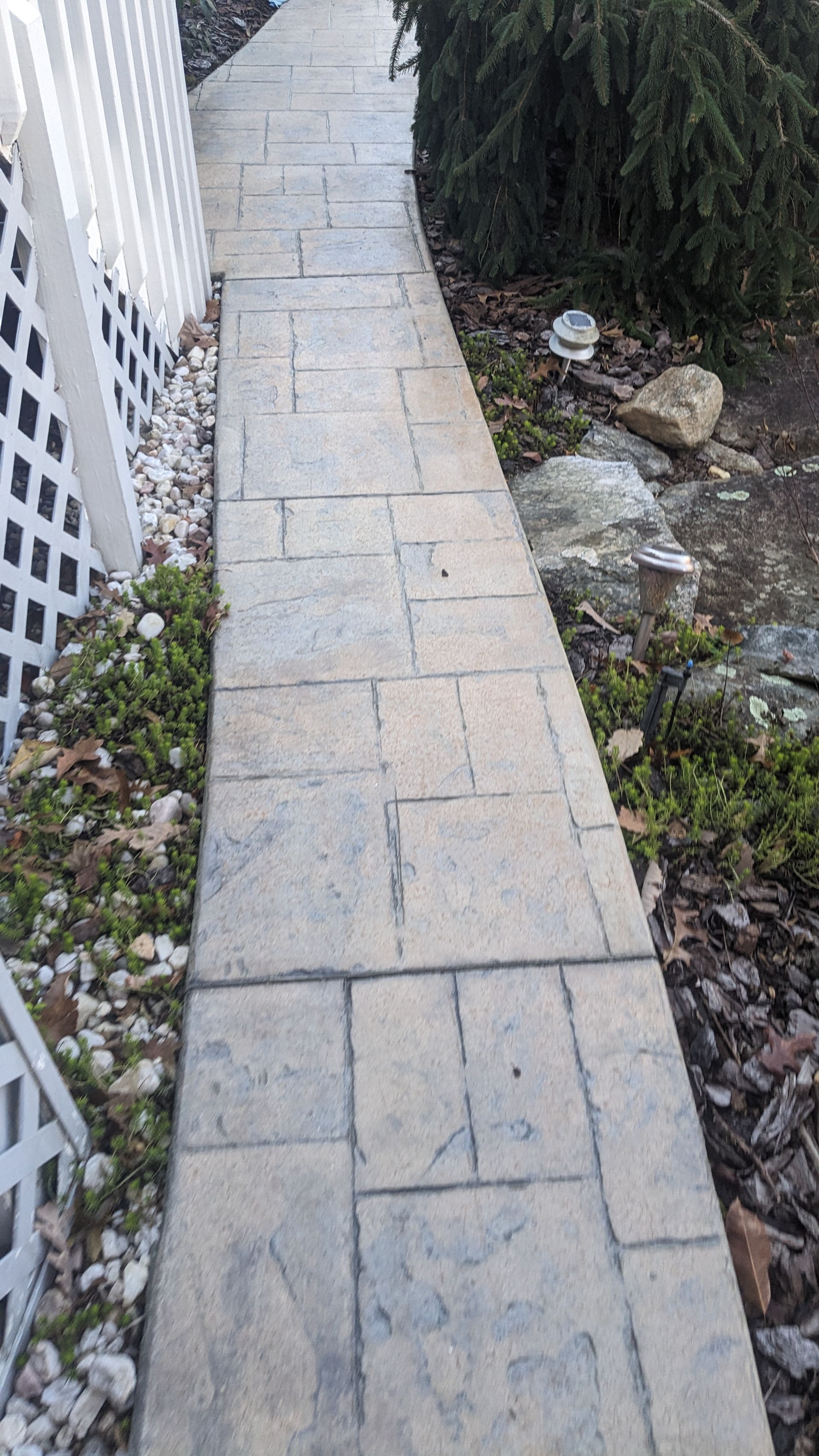 A sidewalk leading to a house with a white fence and rocks.