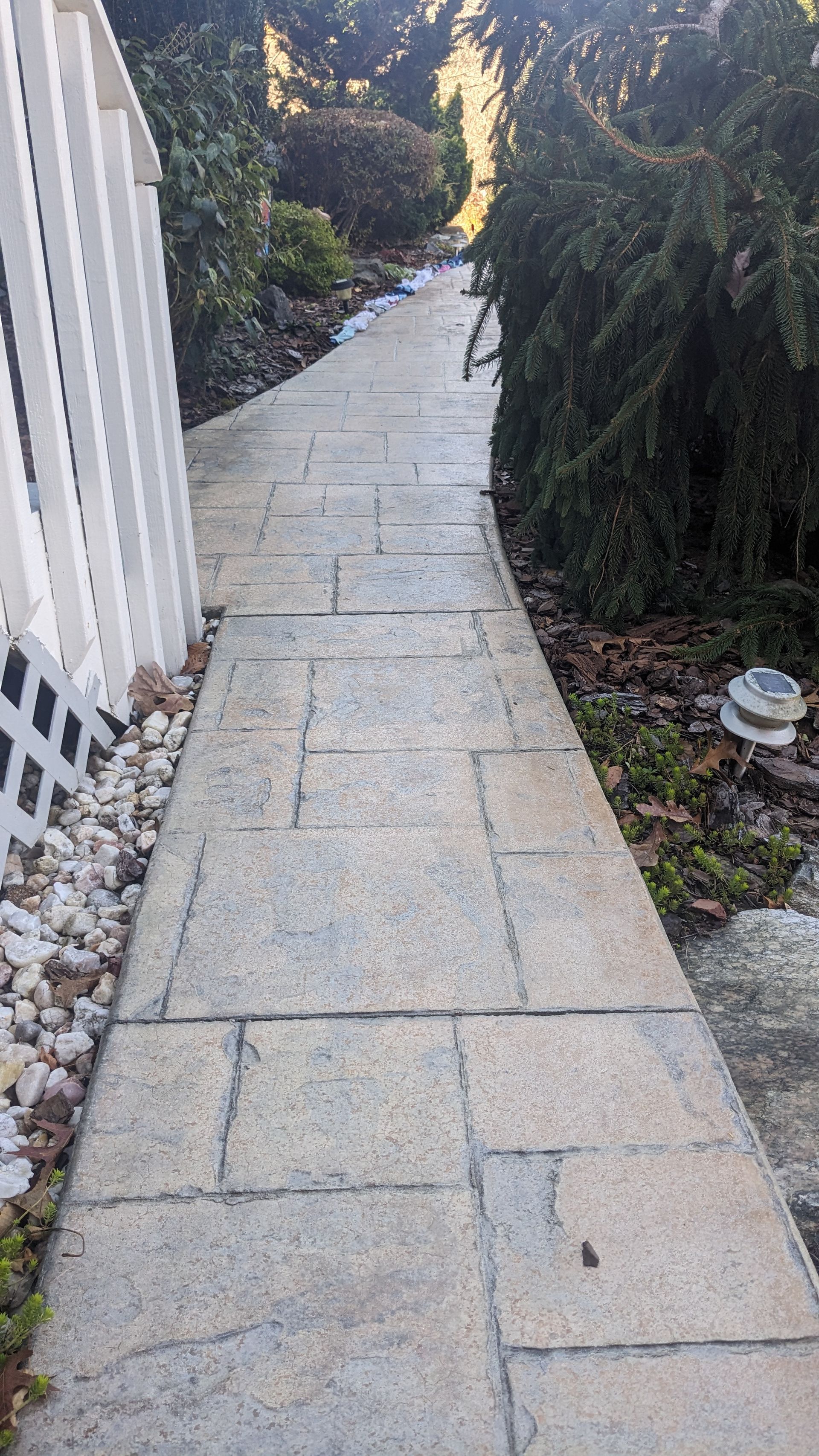 A stone walkway leading to a white fence in a garden.