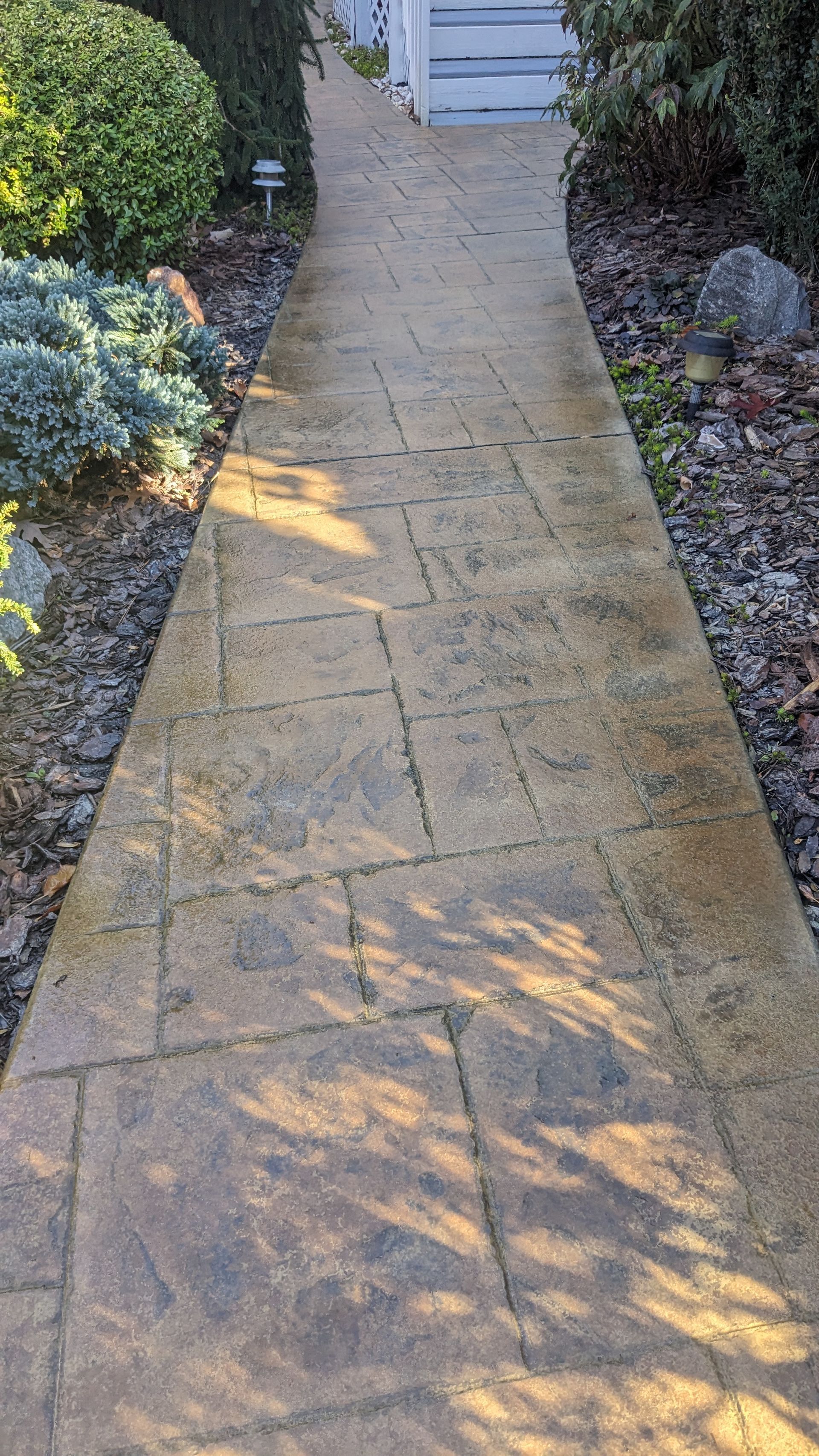 A brick walkway leading to a house in a garden.