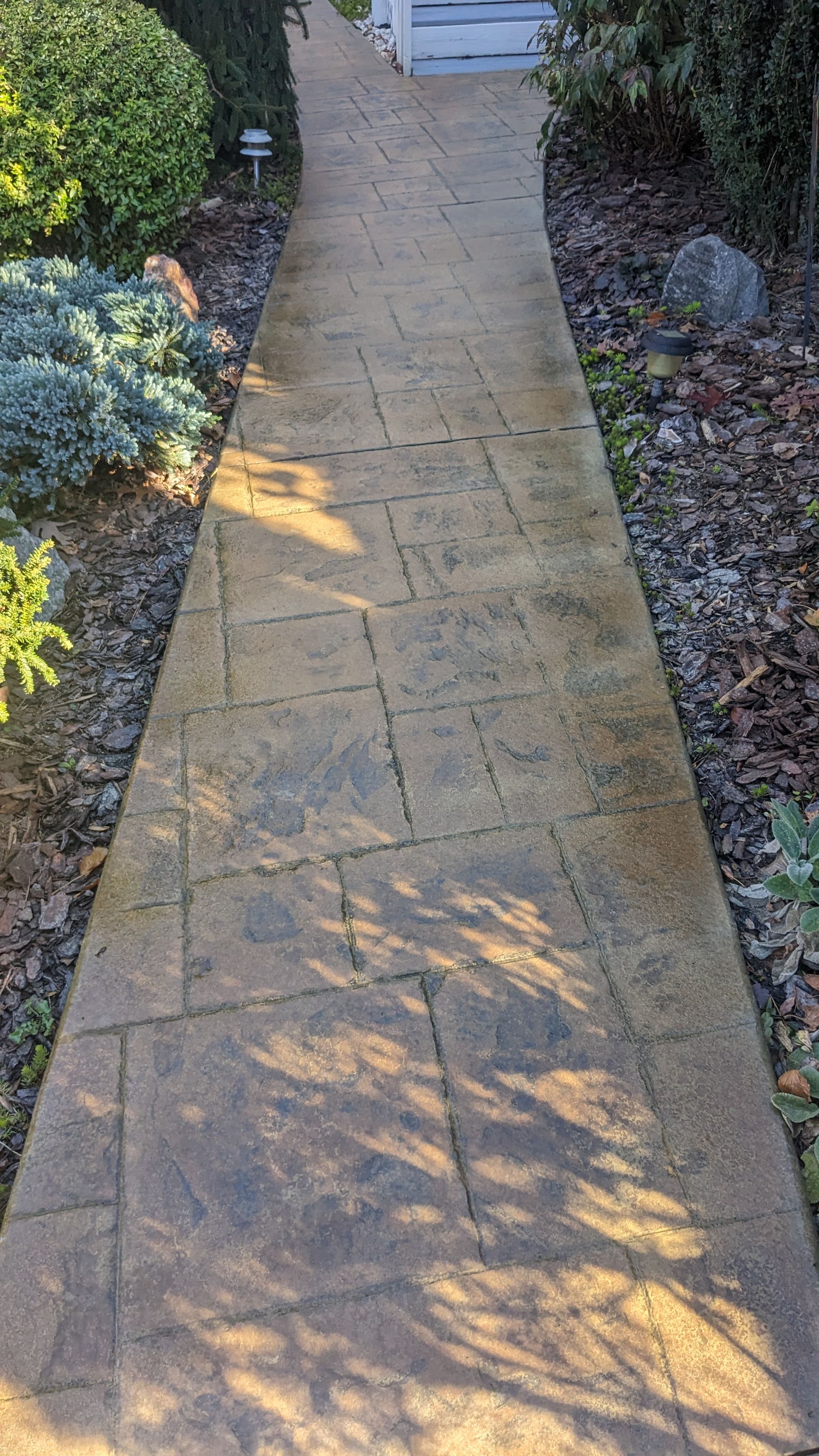 A brick walkway leading to a house in a garden.