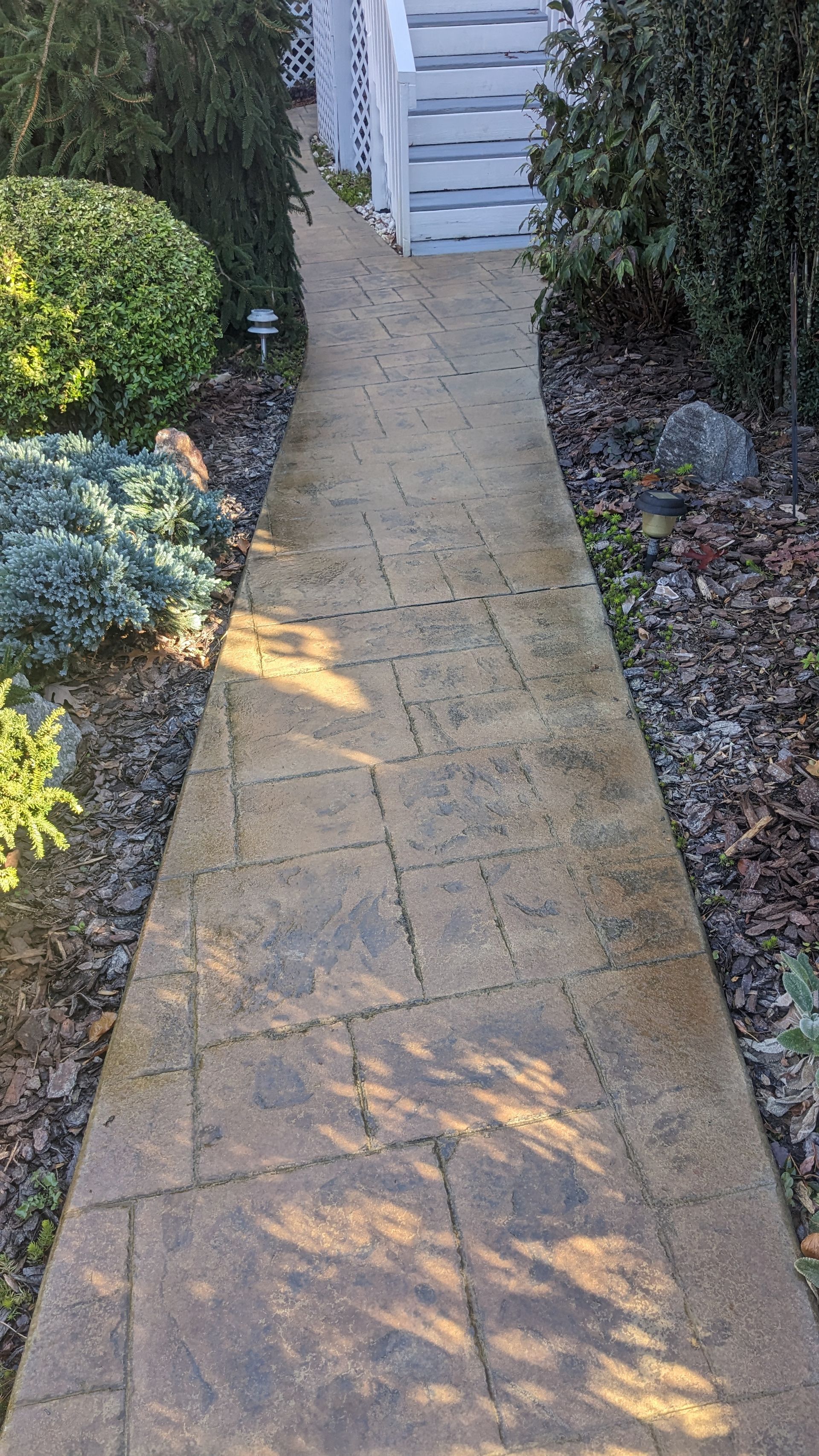 A brick walkway leading to a white house in a garden.