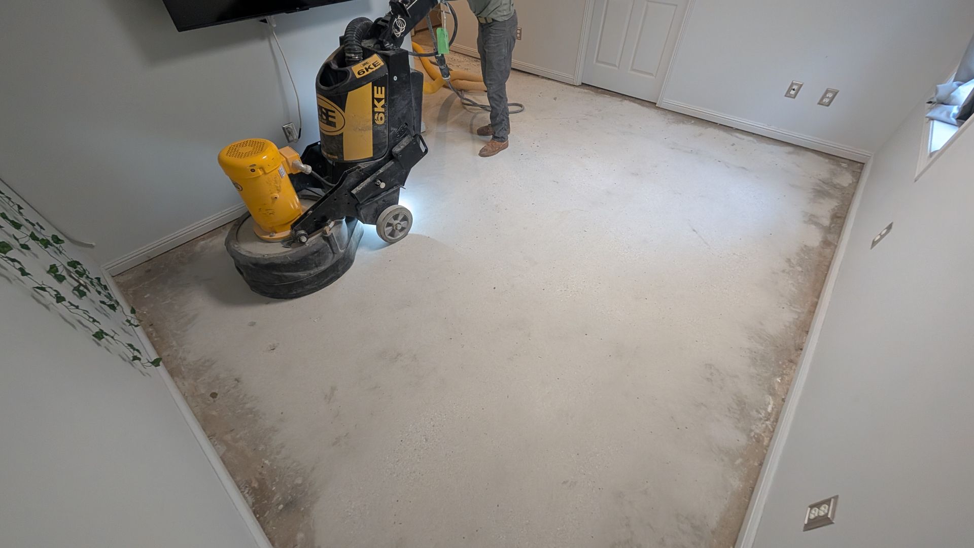 A person is using a grinder on a concrete floor in a room.