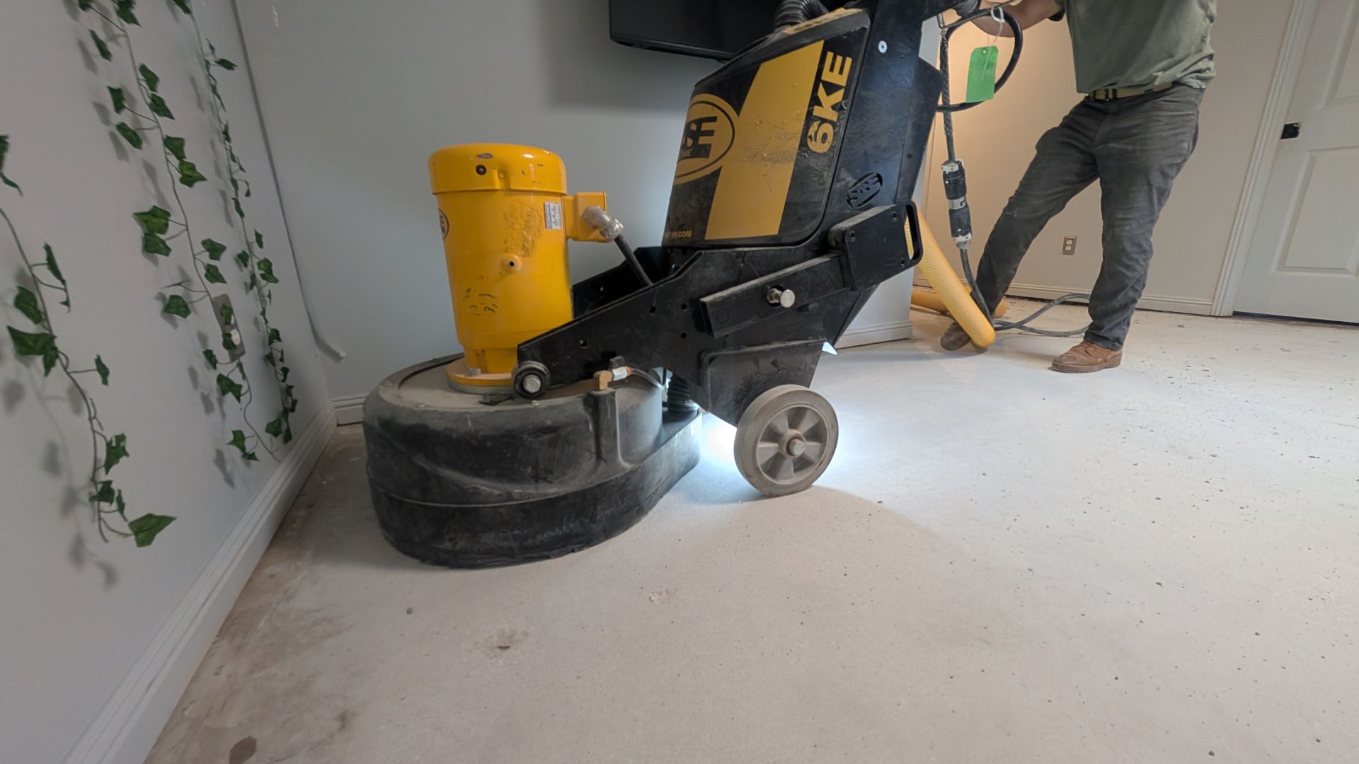 A man is using a grinder on the floor in a room.