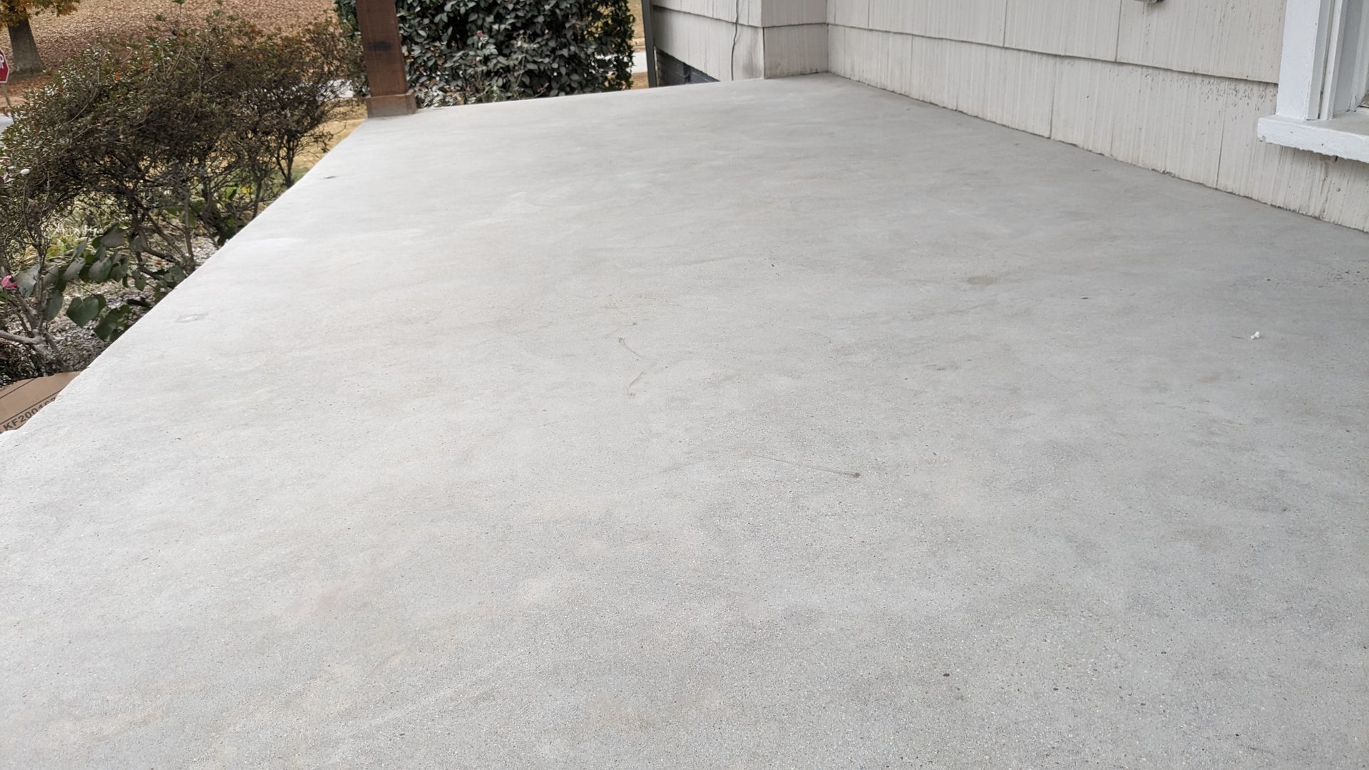 A concrete porch with a white wall and trees in the background.