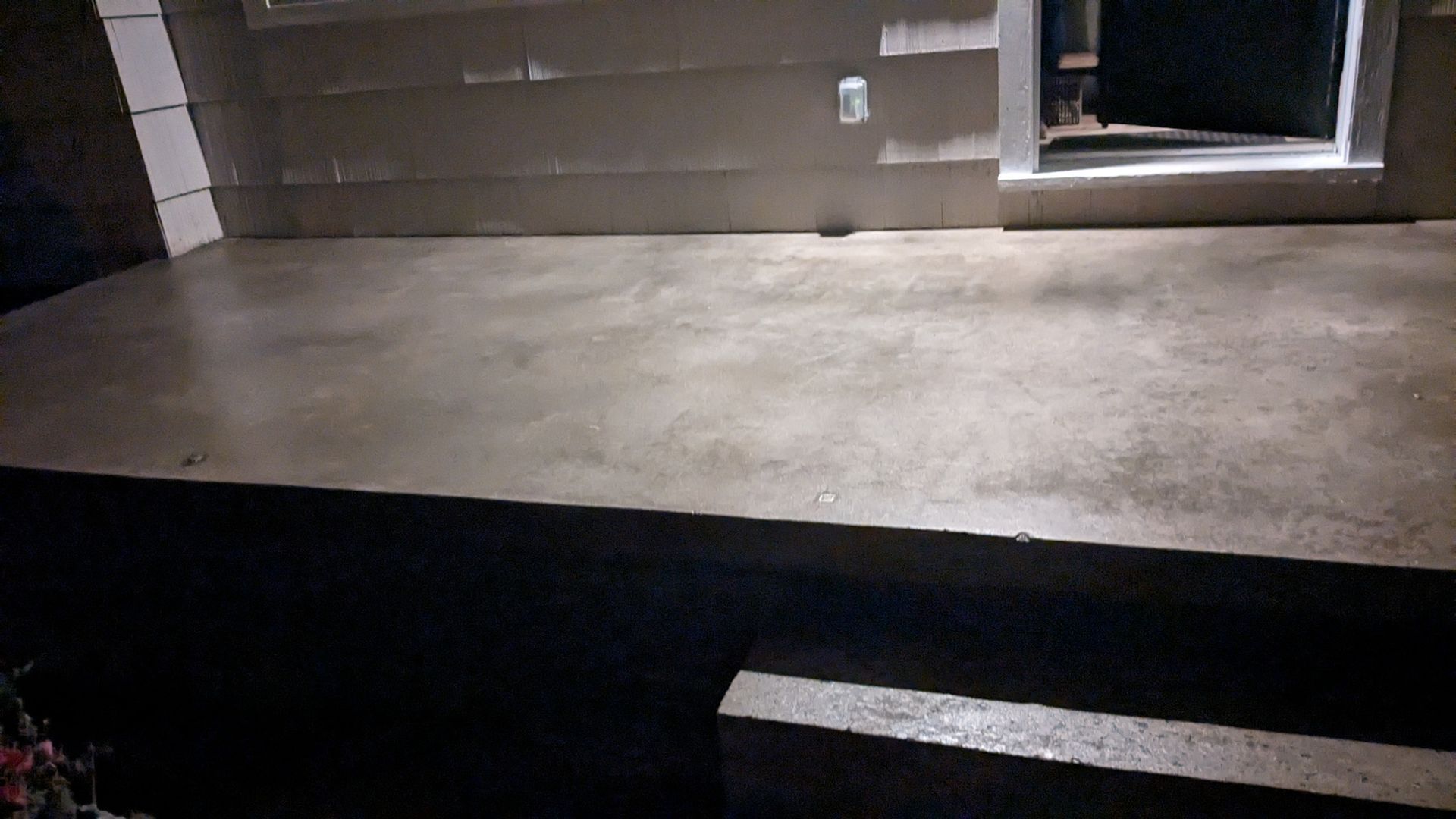 A concrete porch with stairs and a window at night.