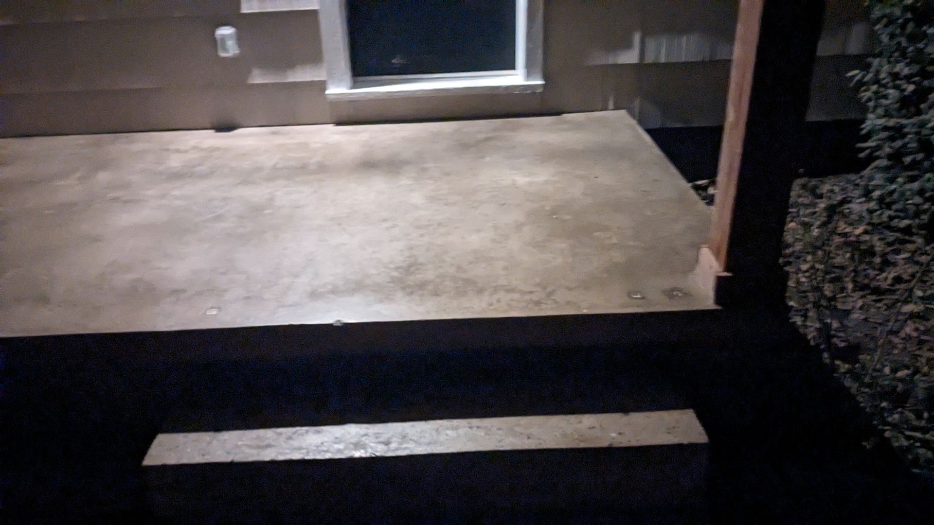 A concrete porch with stairs and a window at night
