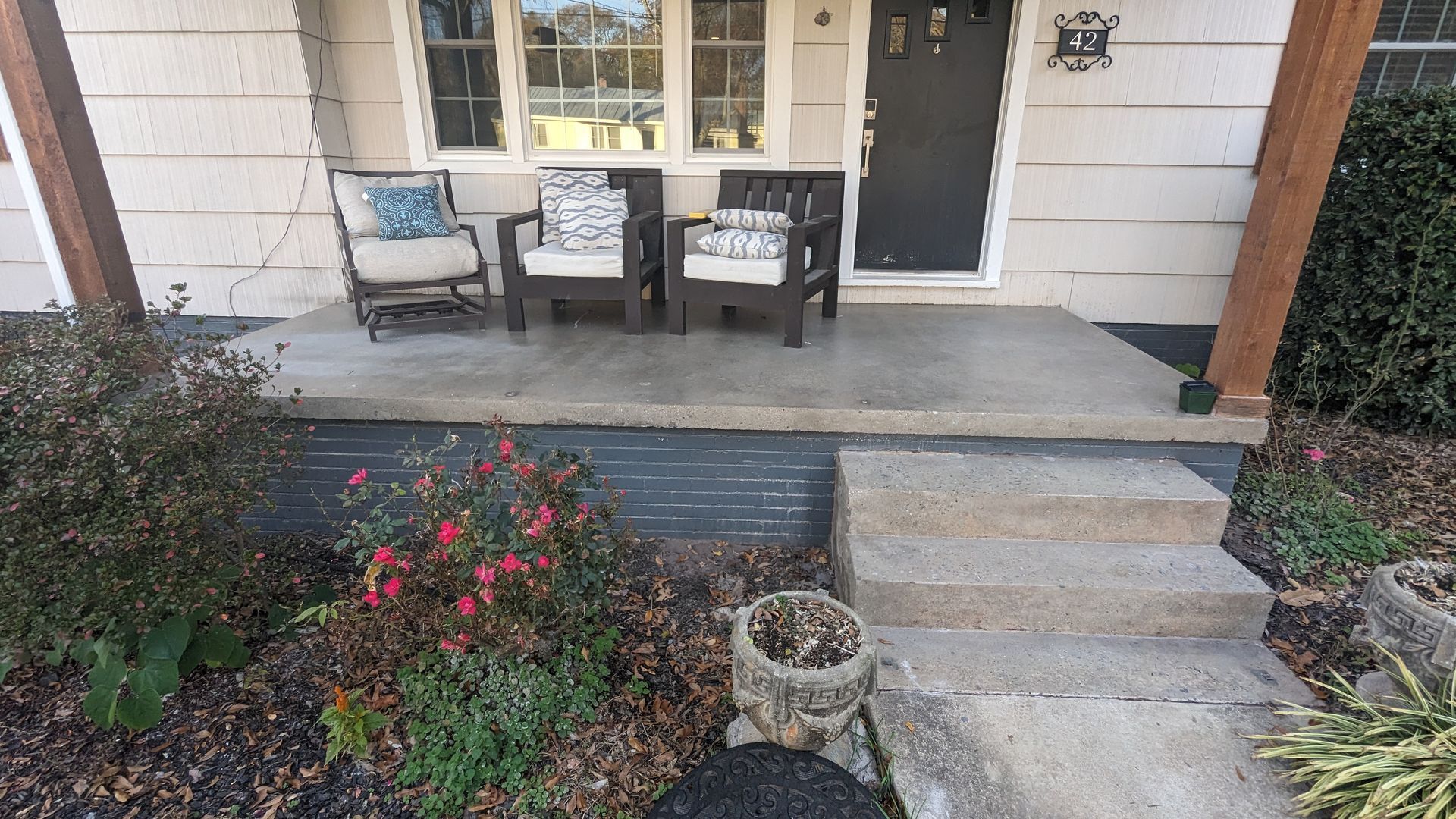 A porch with two chairs and a planter in front of a house.